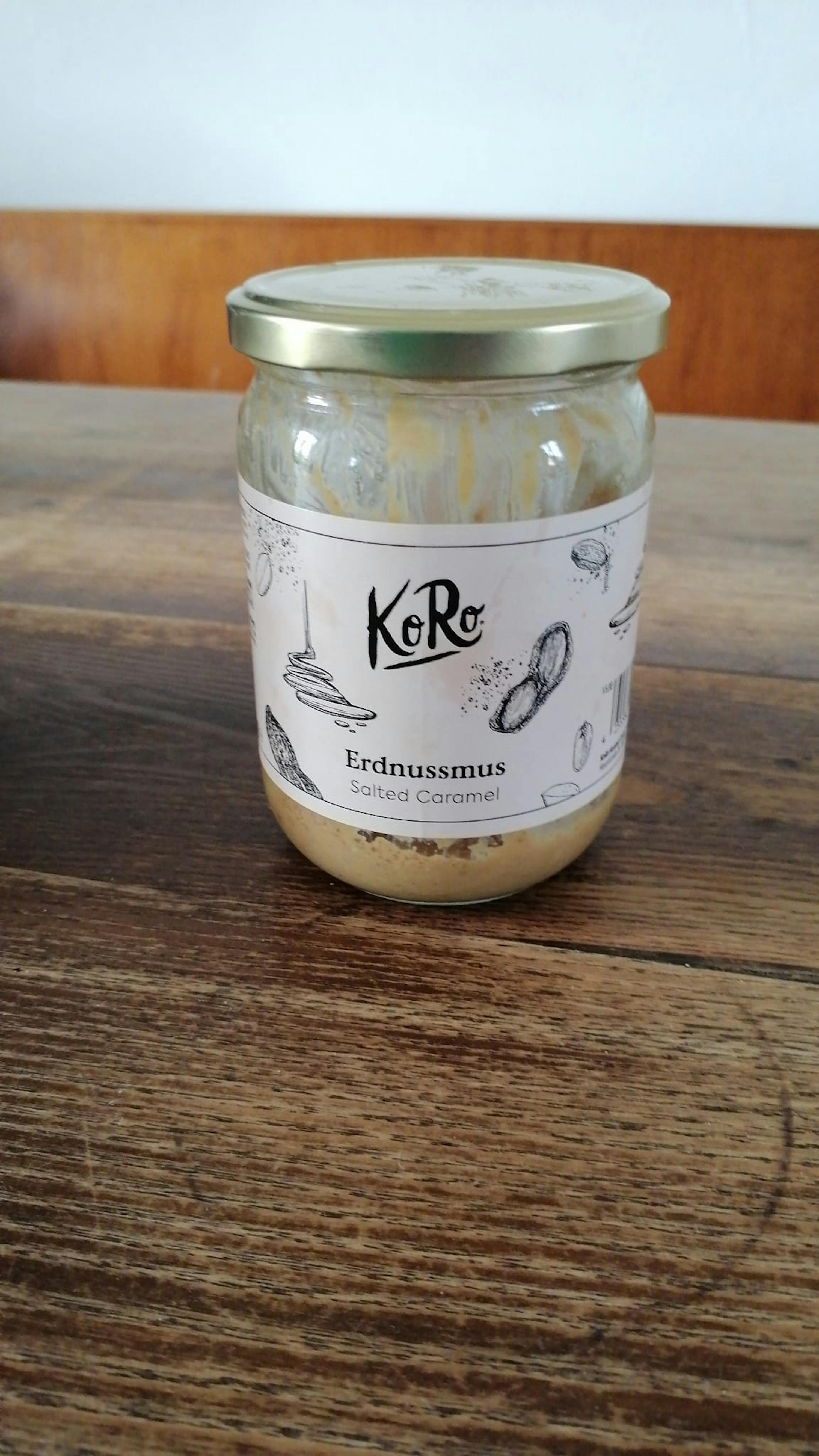 a jar of koro erdnussmus salted caramel sits on a wooden table
