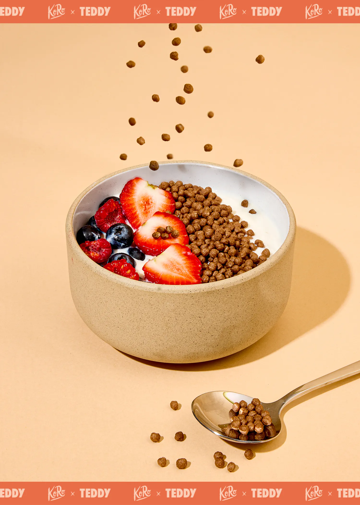 un bol de yaourt avec des fraises, des myrtilles, des framboises et des billes de céréales au chocolat, certaines tombant dans le bol et d'autres sur une cuillère.