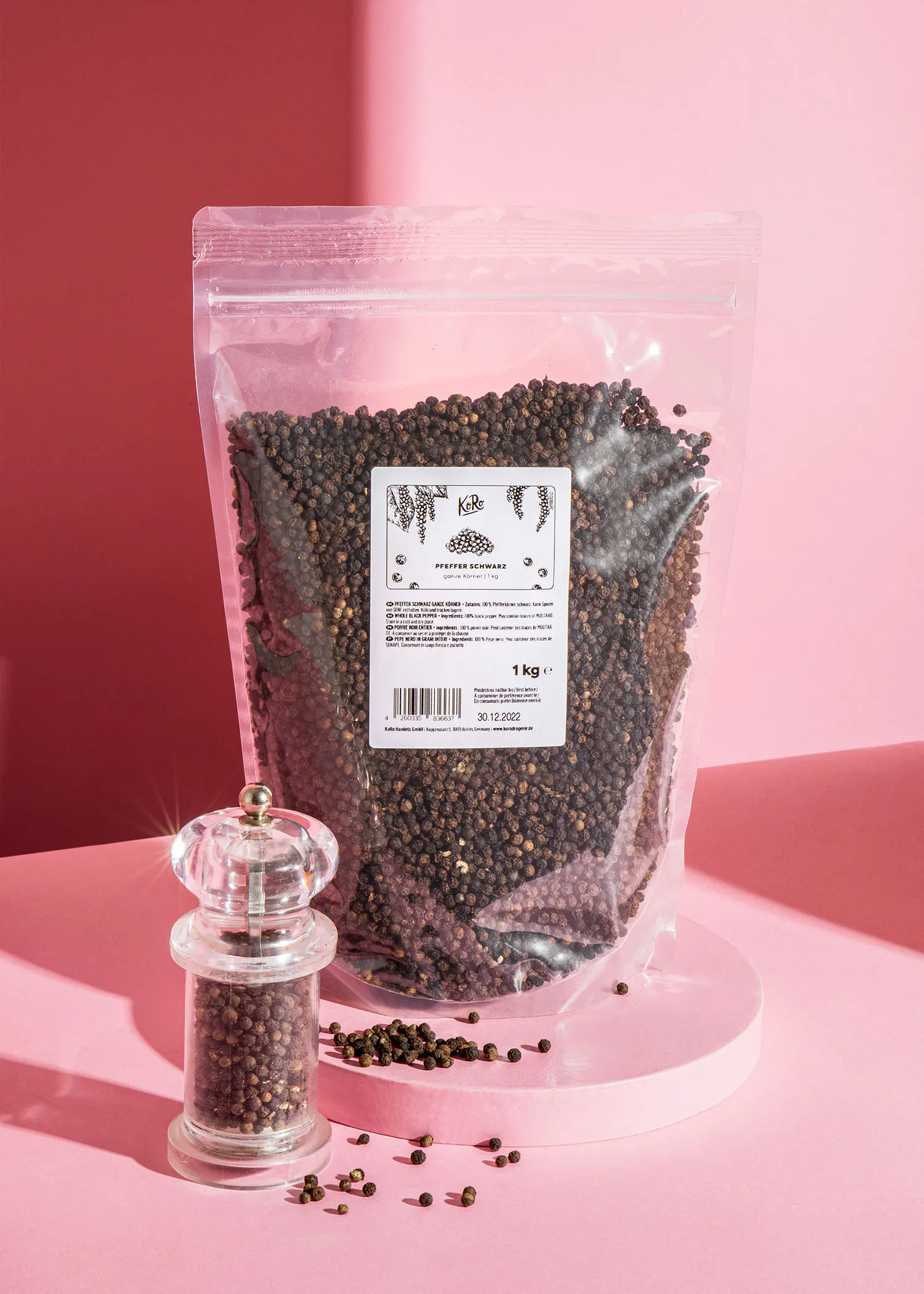 a bag of black pepper sits next to a glass grinder