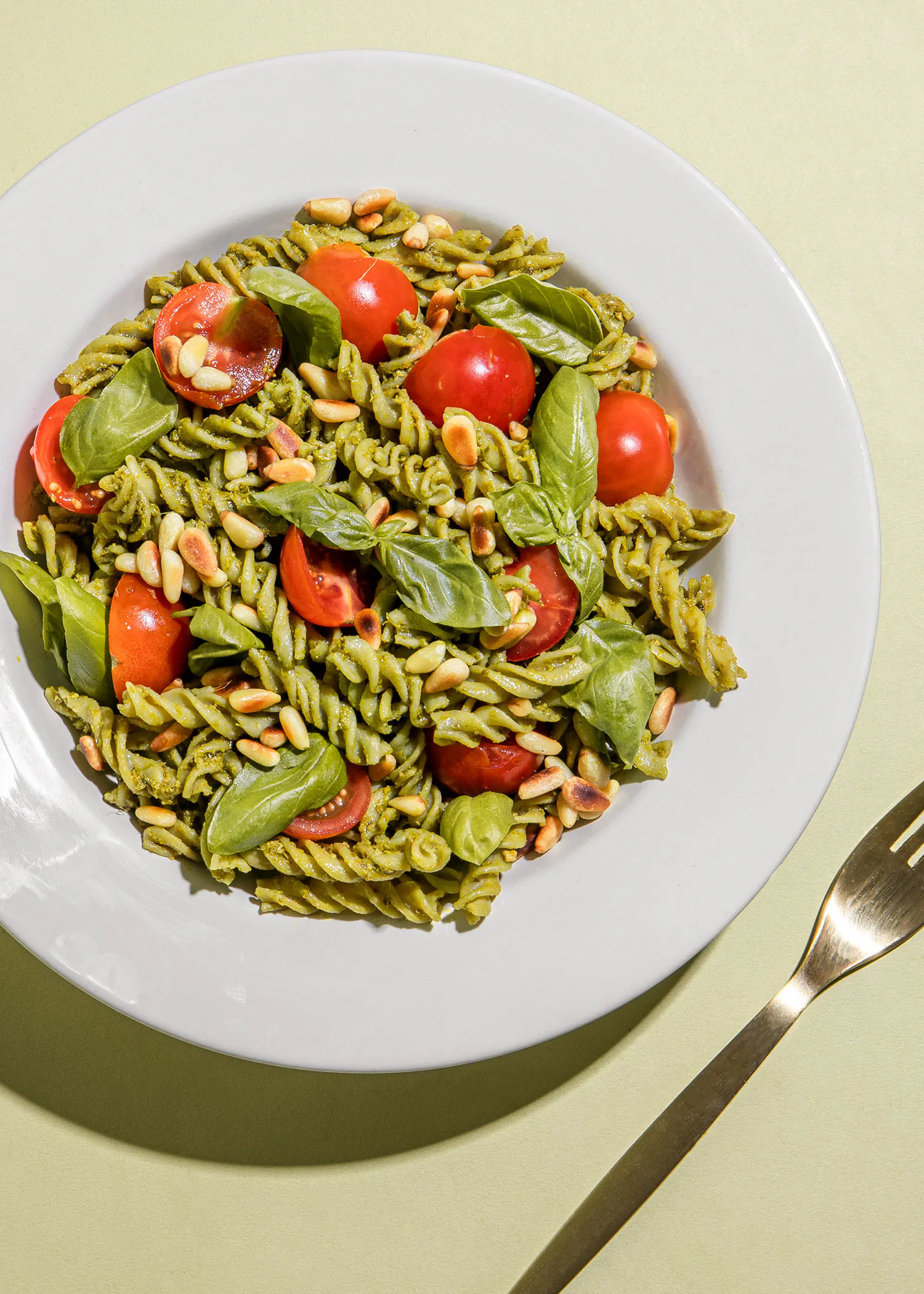 ein weißer Teller mit Nudeln mit Tomaten und Pinienkernen und einer Gabel darauf