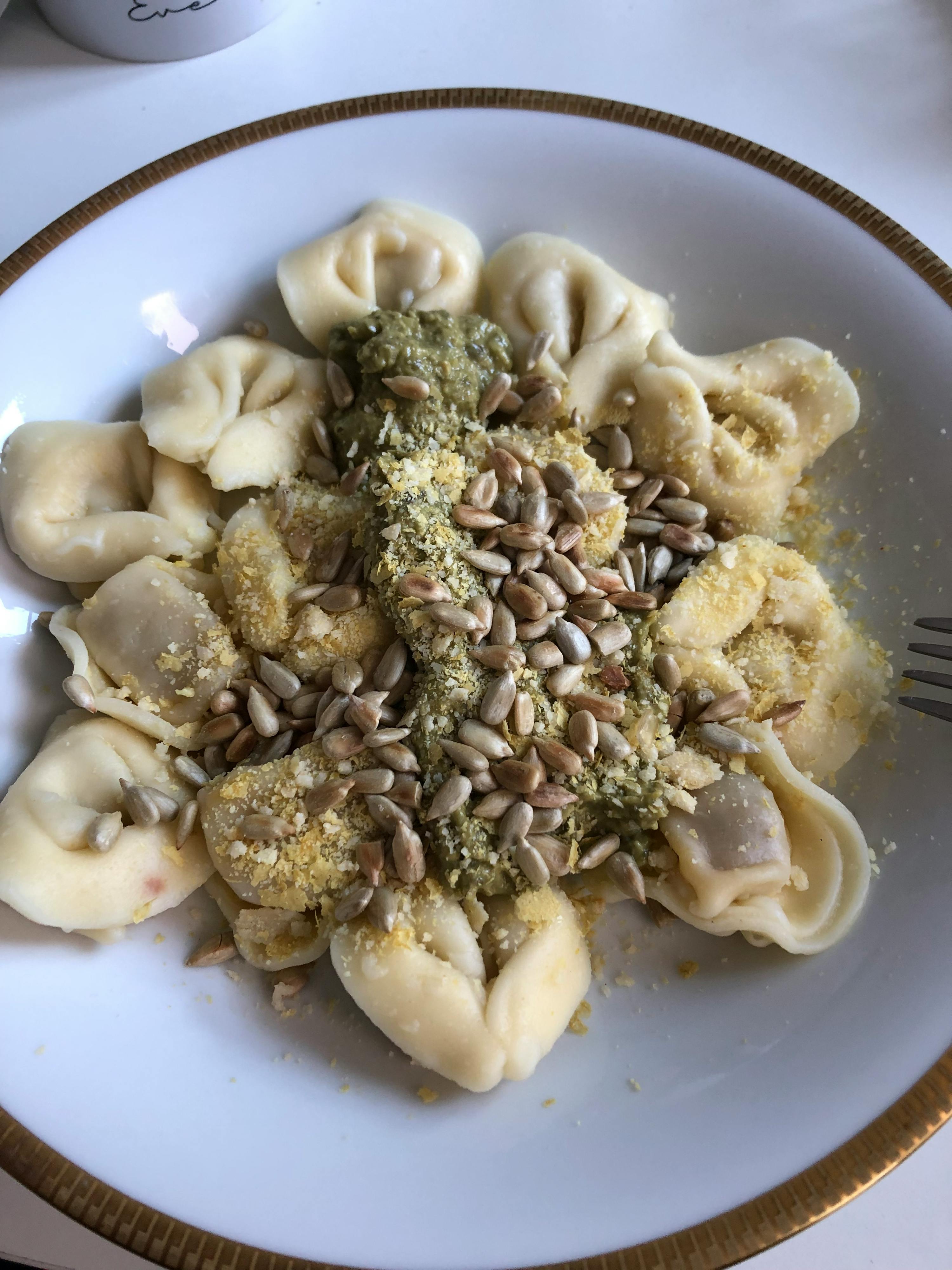a plate of pasta with pesto and sunflower seeds on it