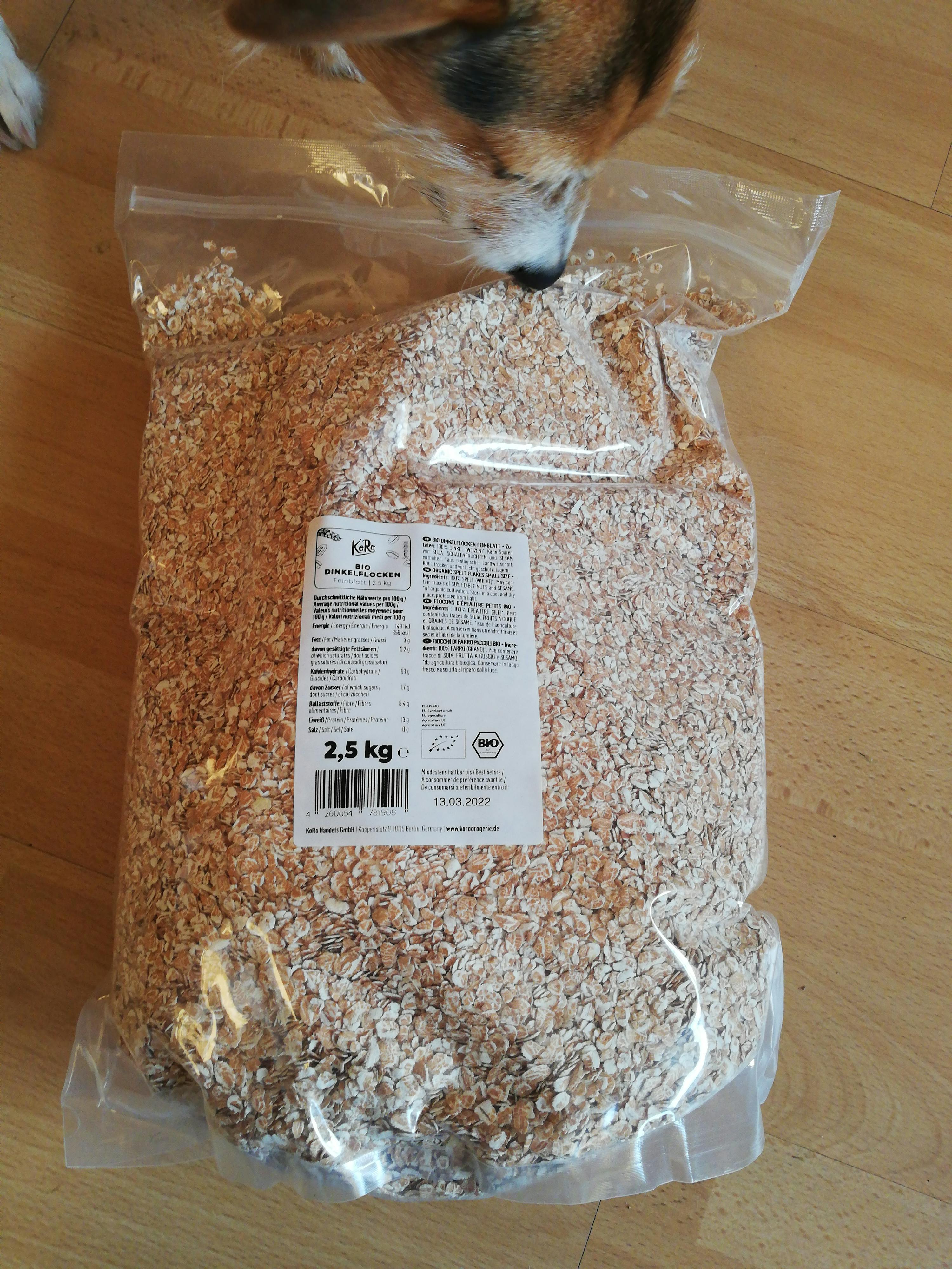 un sacchetto di fiocchi d' avena è su un pavimento di legno accanto a un cane