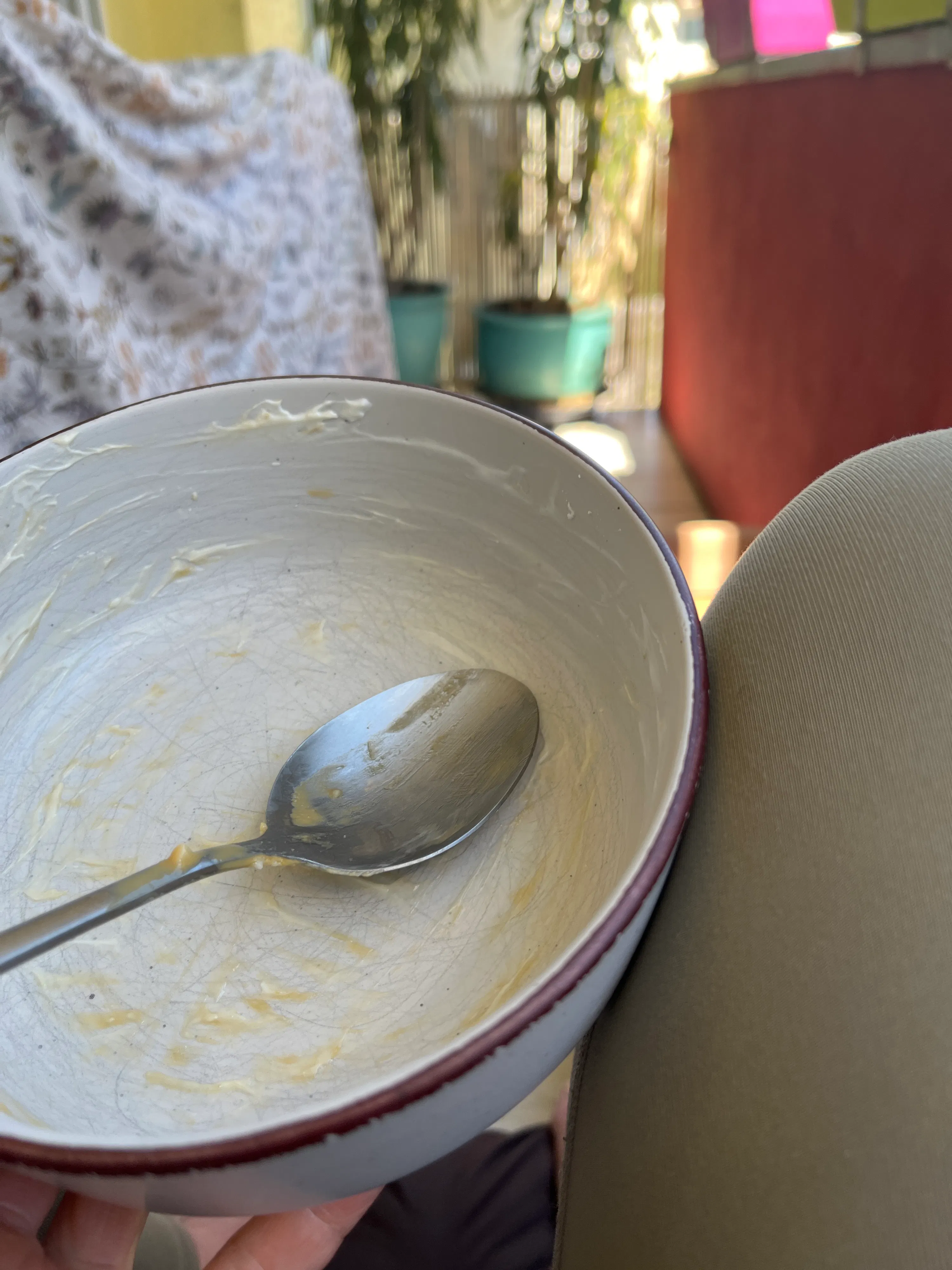 an empty bowl with a spoon and yellowish food remnants is held up, with a blurry outdoor background.