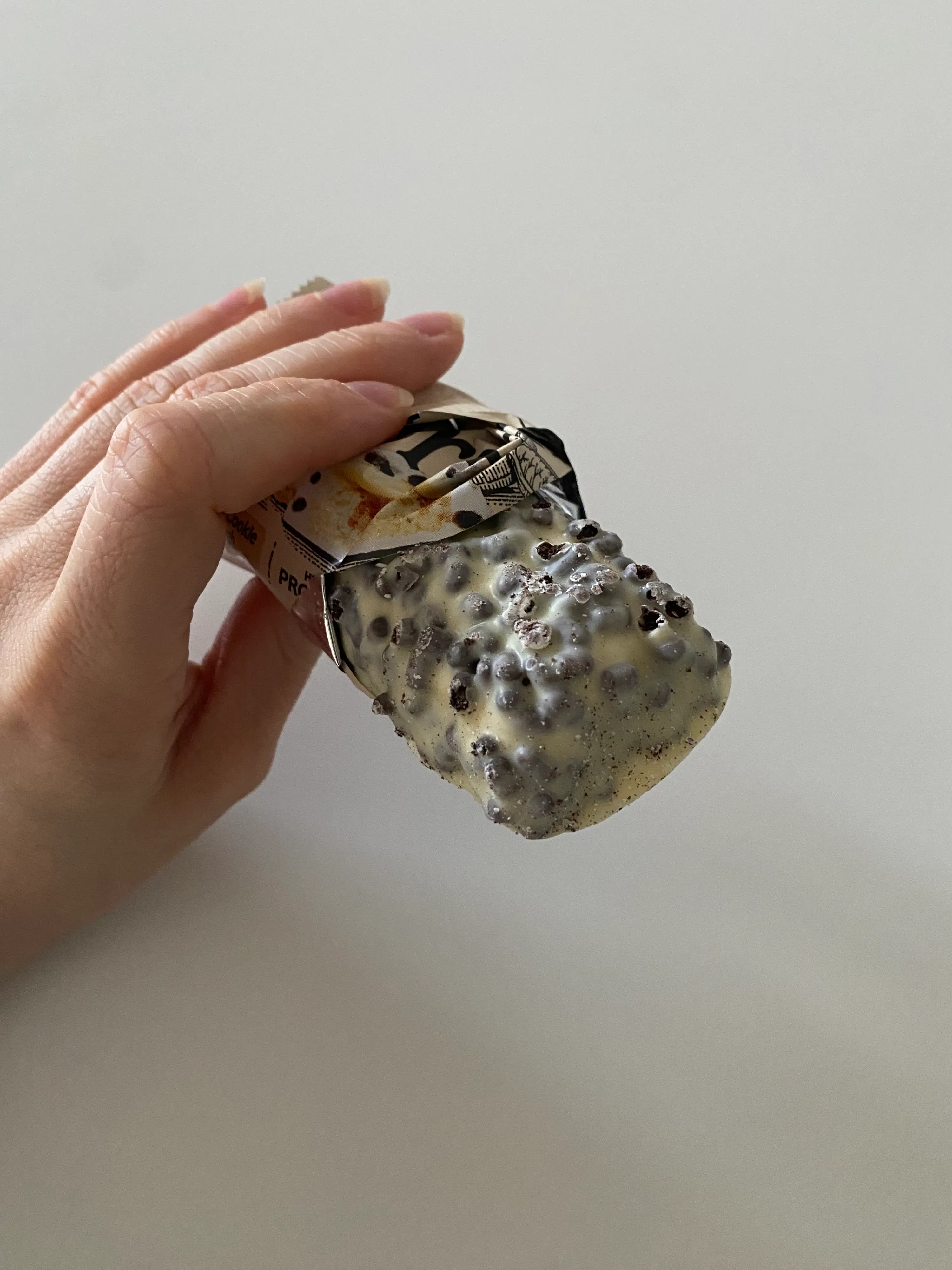 una mano tiene una barretta snack parzialmente scartata con una copertura bianca e pezzetti scuri.