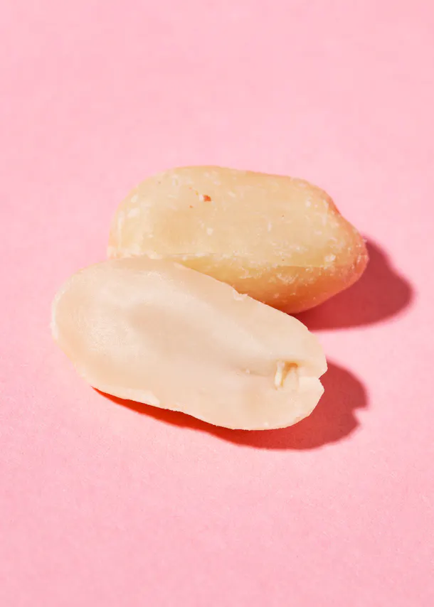 eine Erdnuss , die auf einem rosa Hintergrund in zwei Hälften geschnitten ist