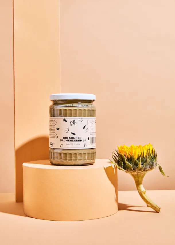 ein Glas Sonnenblumenkernmus steht neben einer Sonnenblume