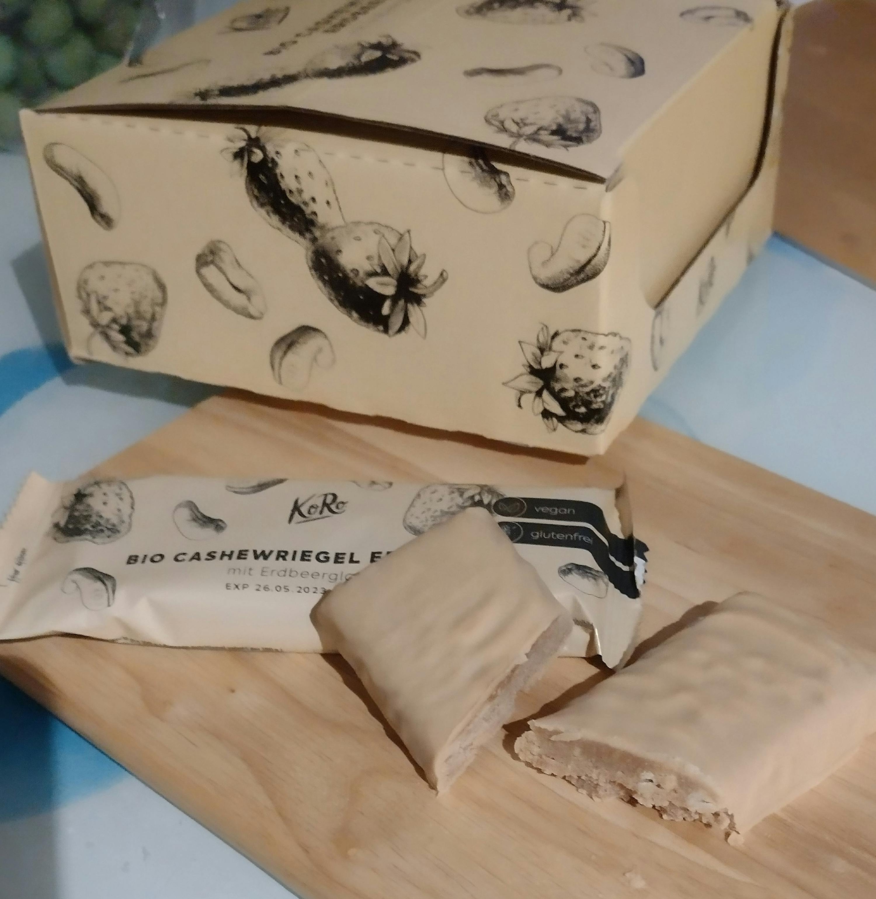 une boîte avec des fraises et des noix de cajou est assise sur une planche à découper en bois