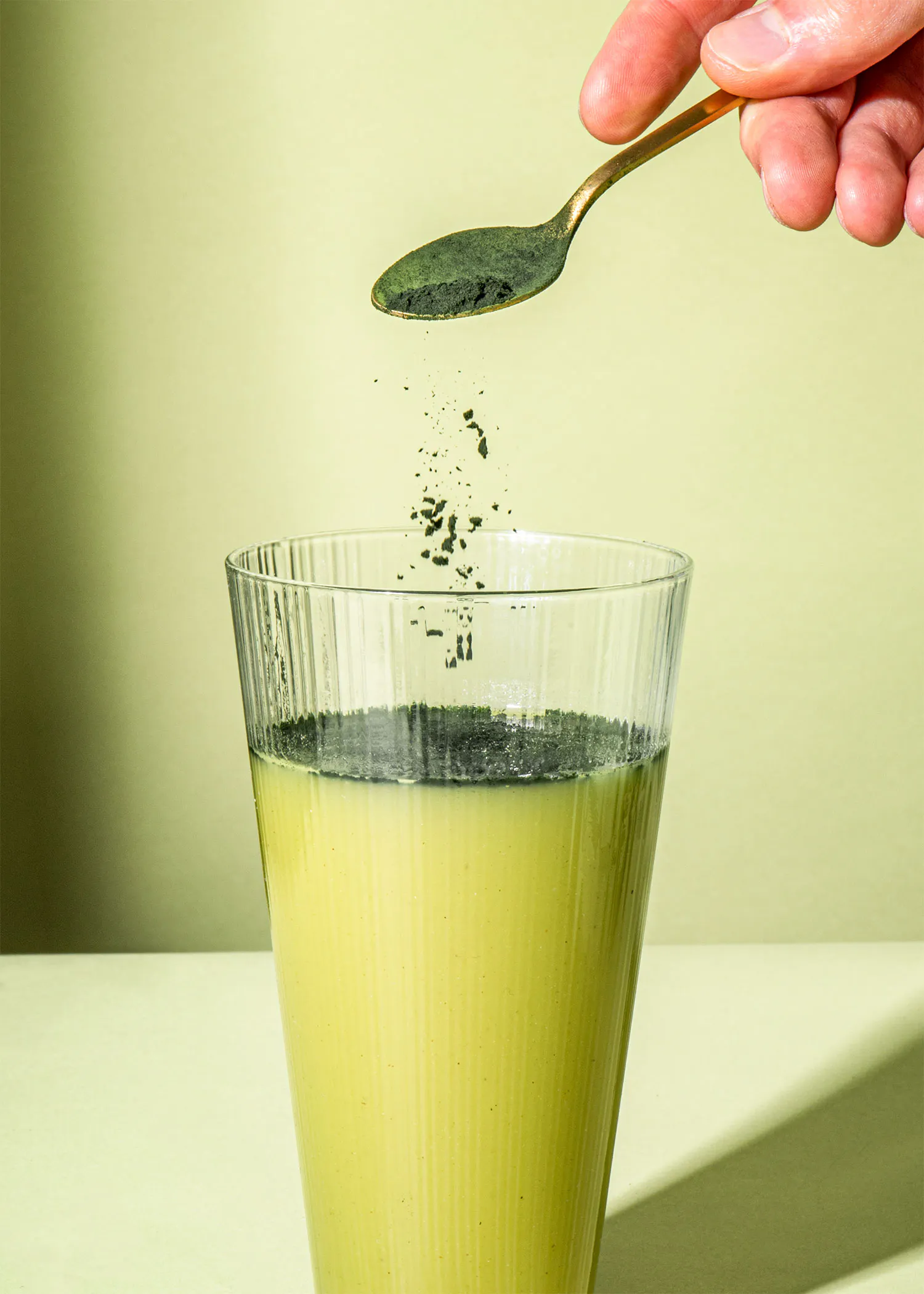 une personne verse une cuillère de poudre verte dans un verre de liquide