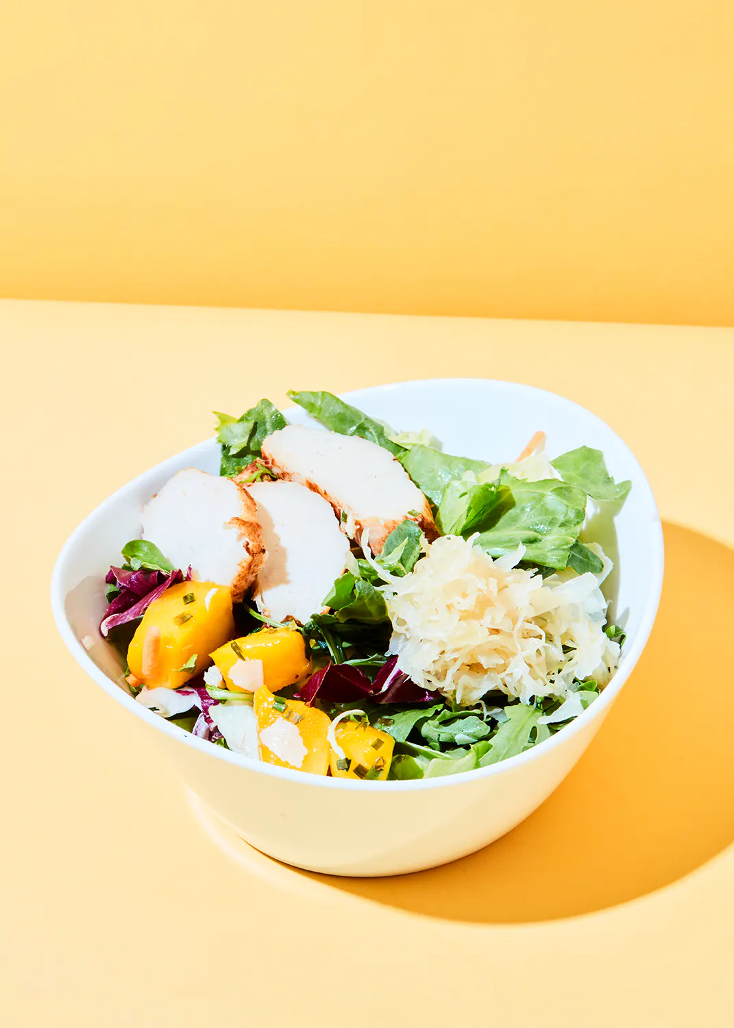 un bol blanc rempli d' une salade avec du poulet et des légumes