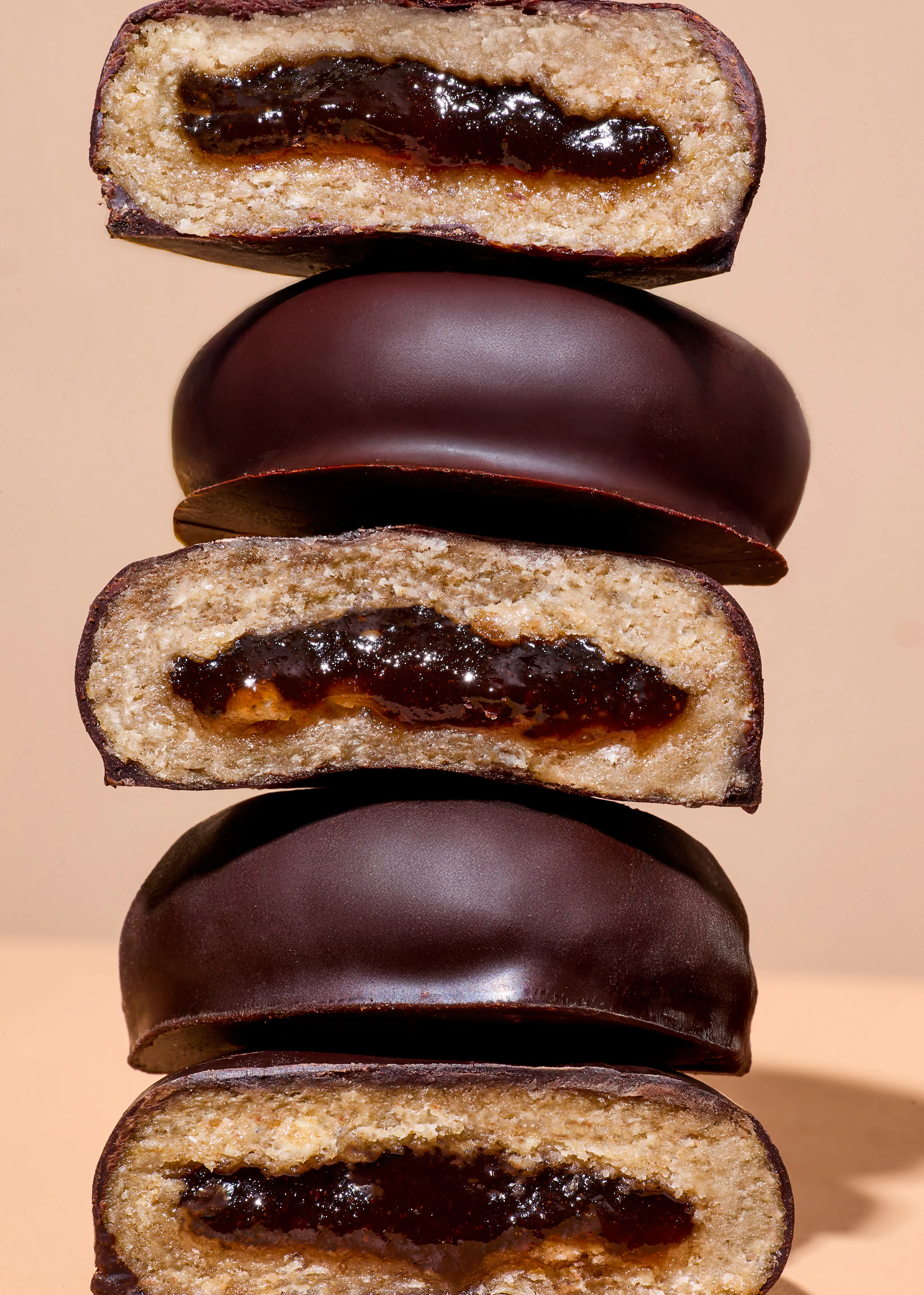 ein stapel schokoladenkekse, von denen einige halbiert sind und eine dunkle, fruchtige füllung zeigen.
