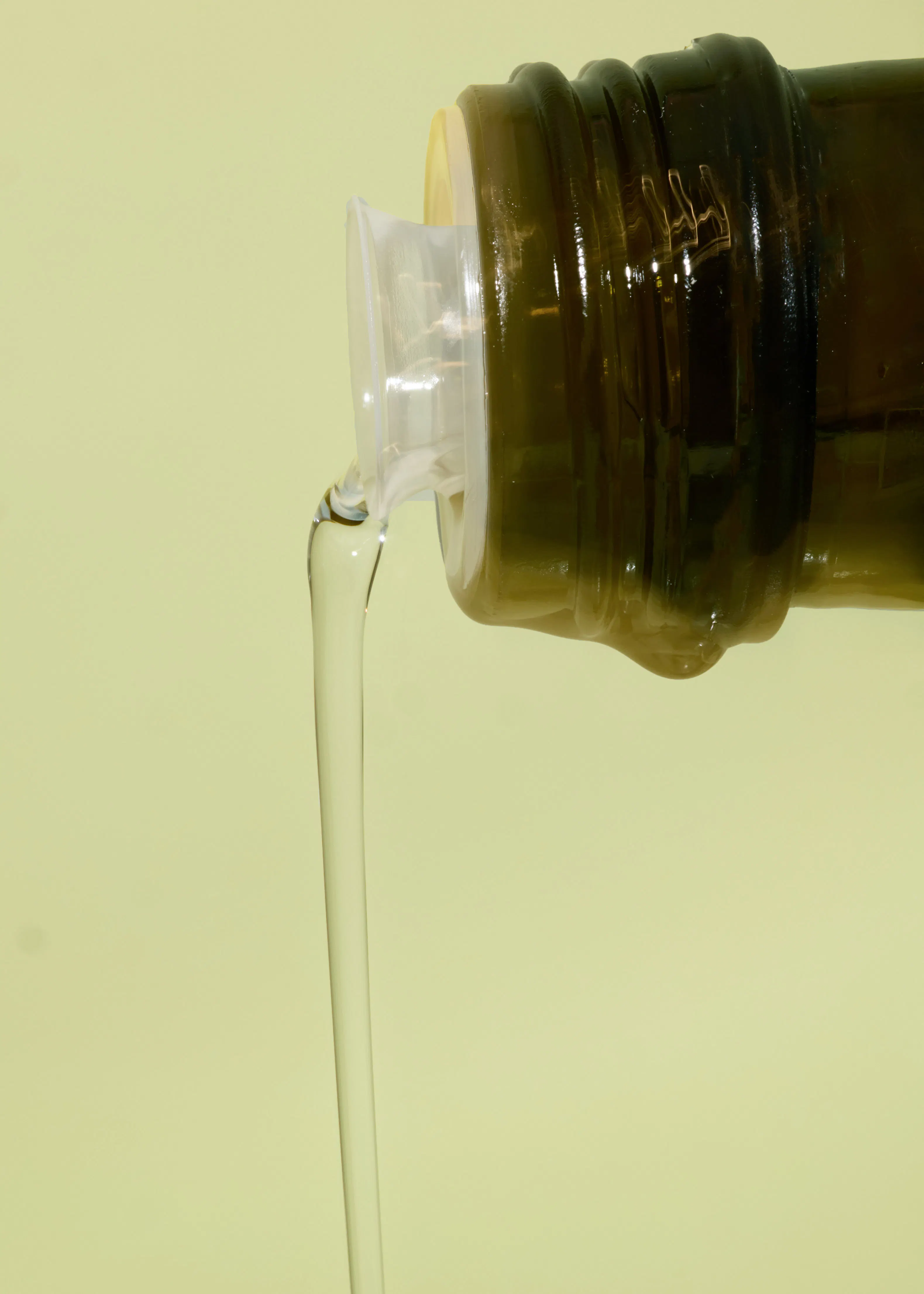 a bottle of olive oil is being poured into a glass container