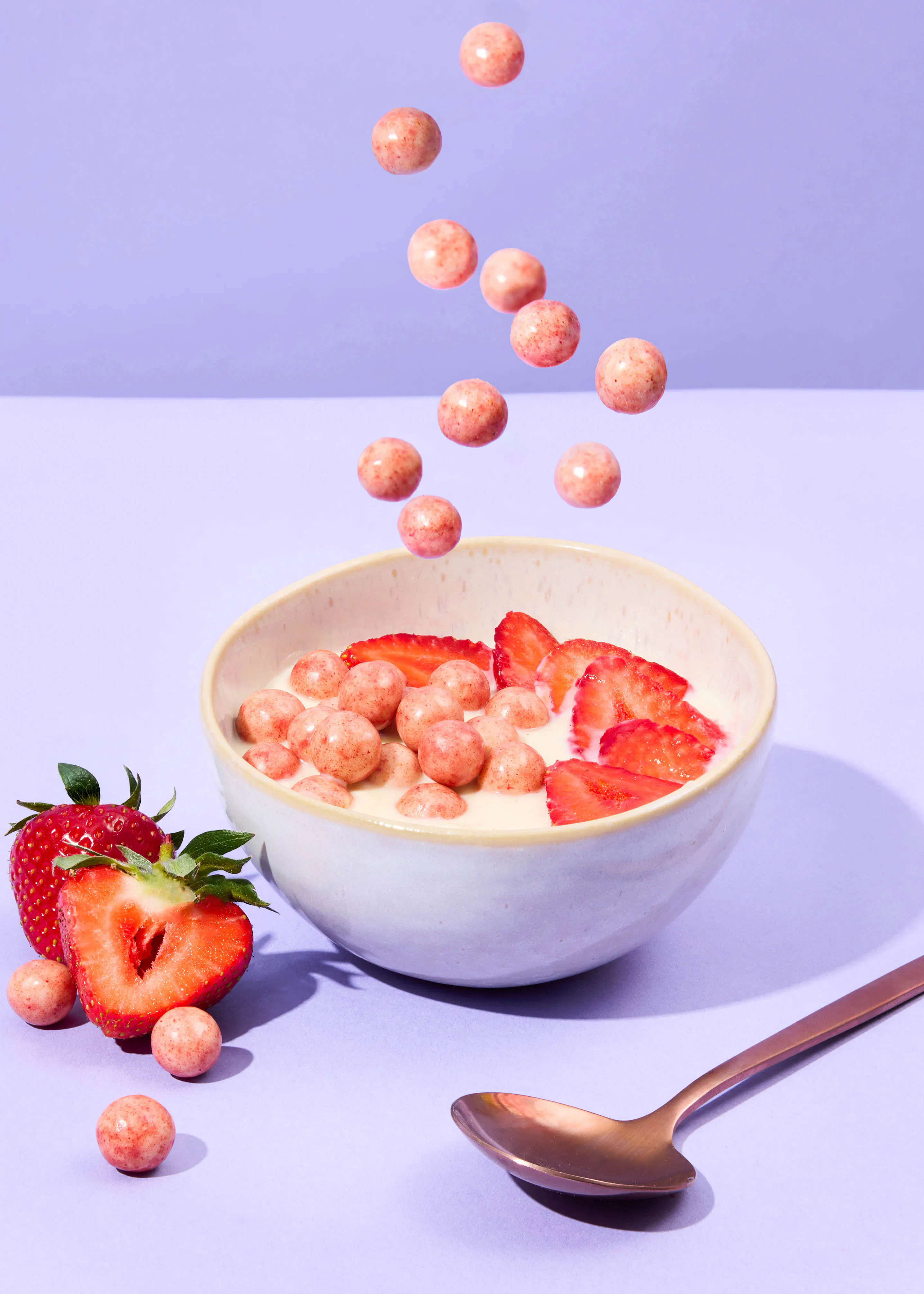 un bol de céréales avec des fraises et une cuillère sur une table violette