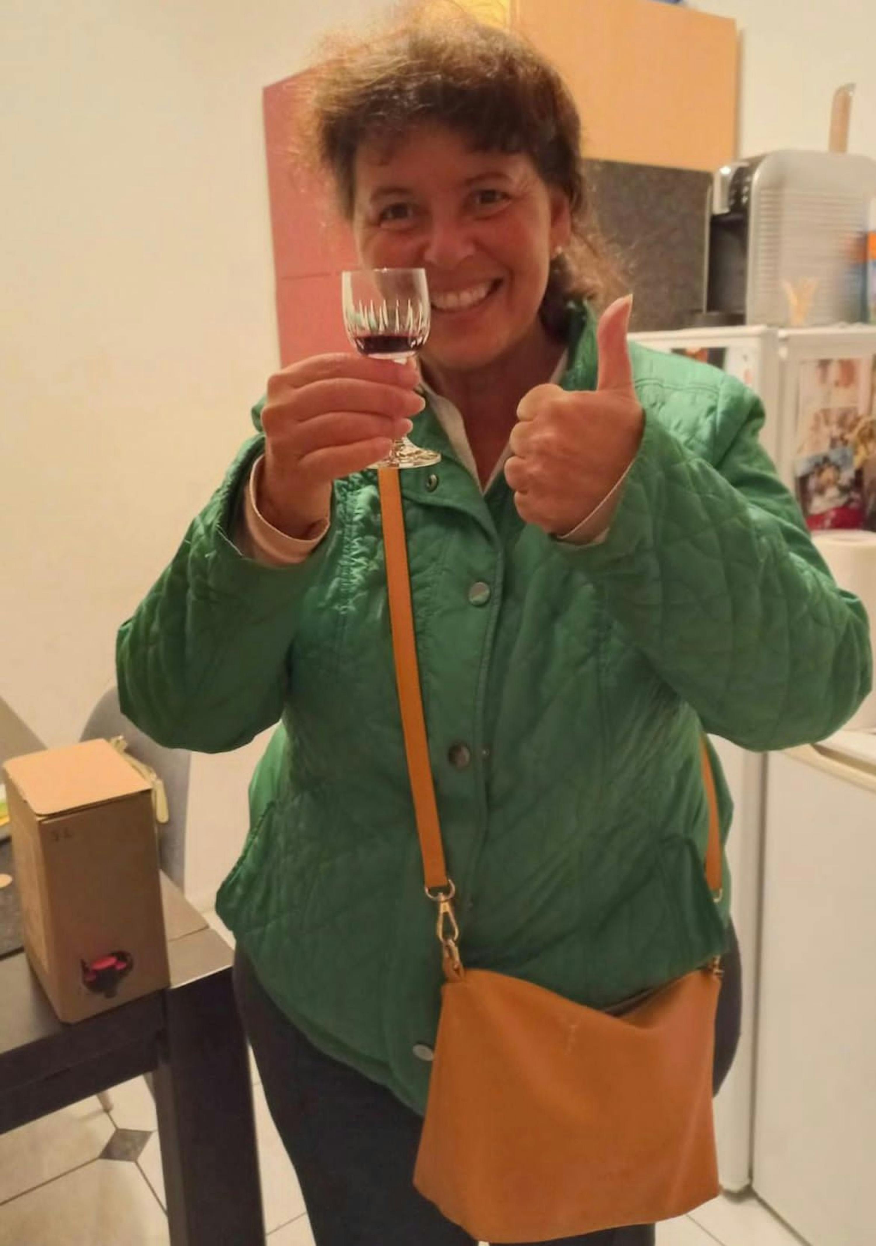 une femme en veste verte tient un verre de vin rouge et donne un coup de pouce