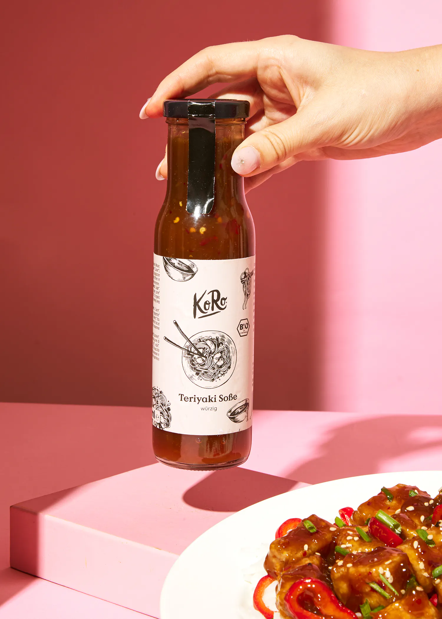 une personne tient une bouteille de sauce teriyaki près d' une assiette de nourriture