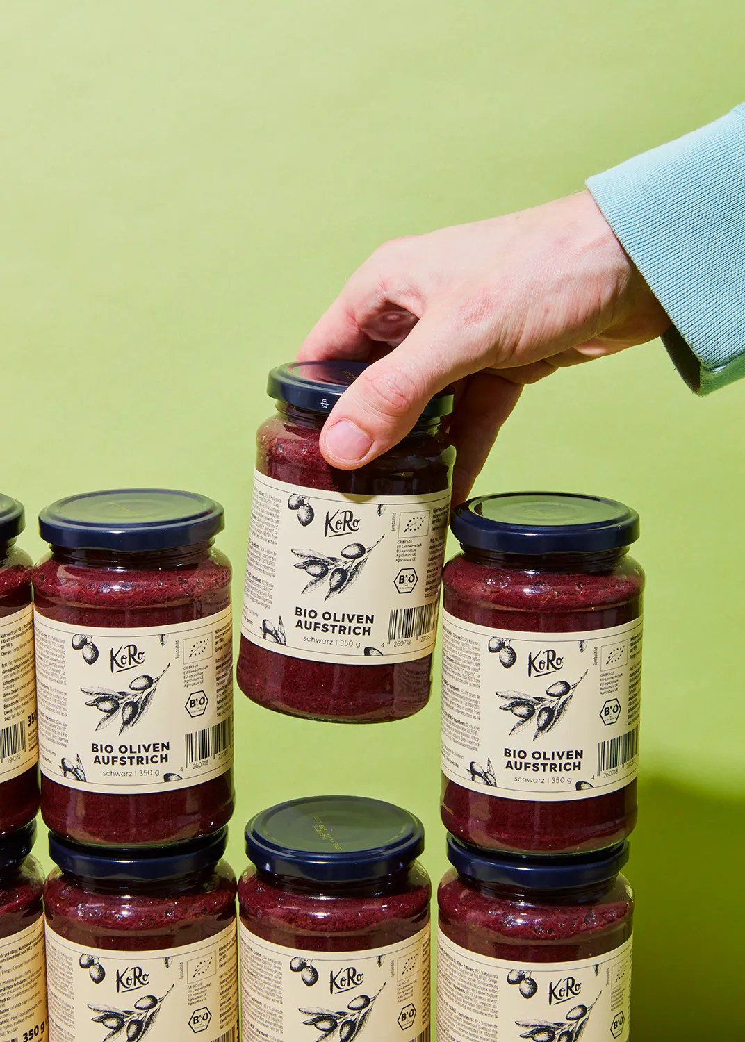 eine hand hält ein glas bio oliven aufstrich