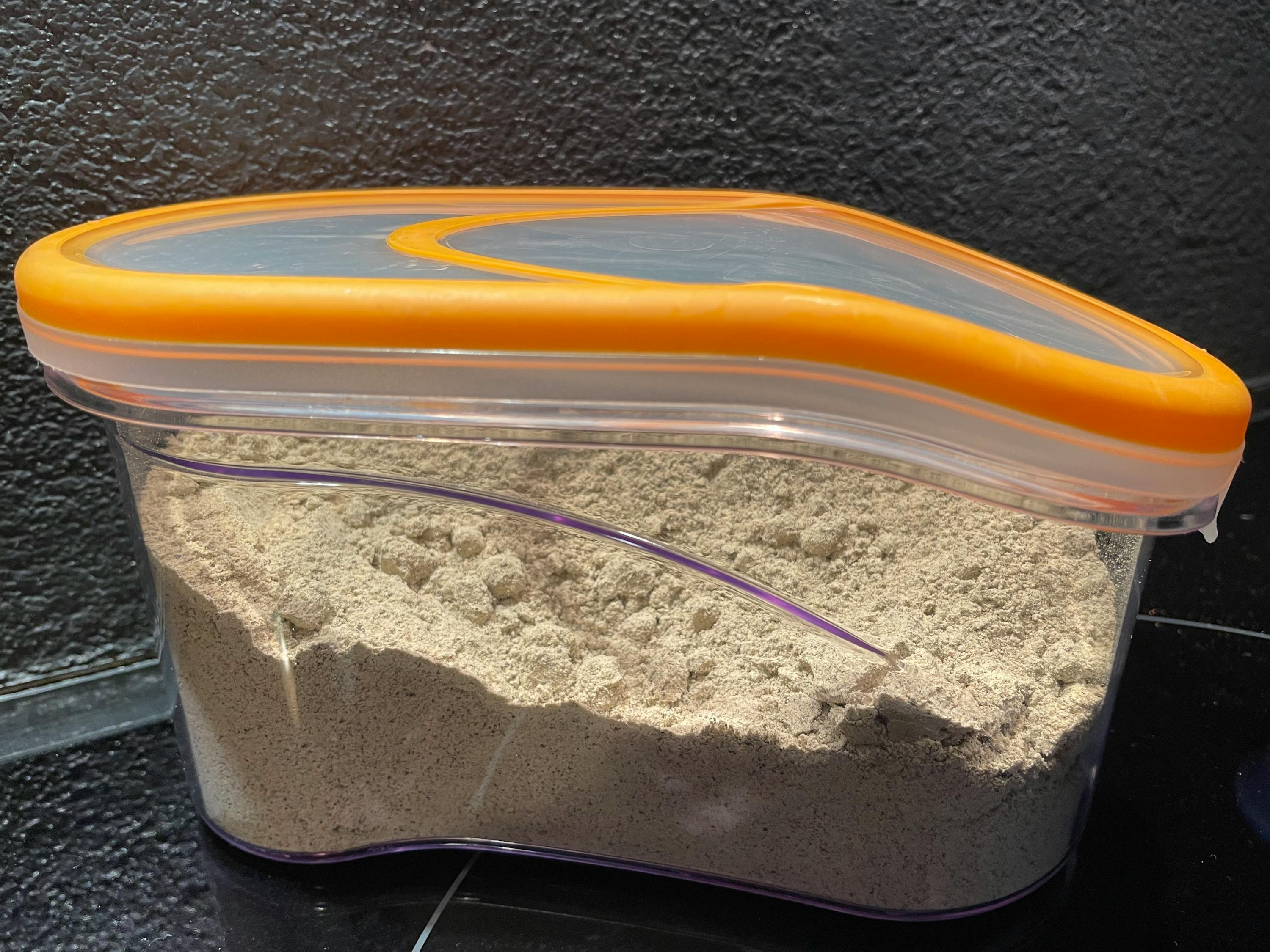un contenitore di plastica con un coperchio arancione è pieno di farina