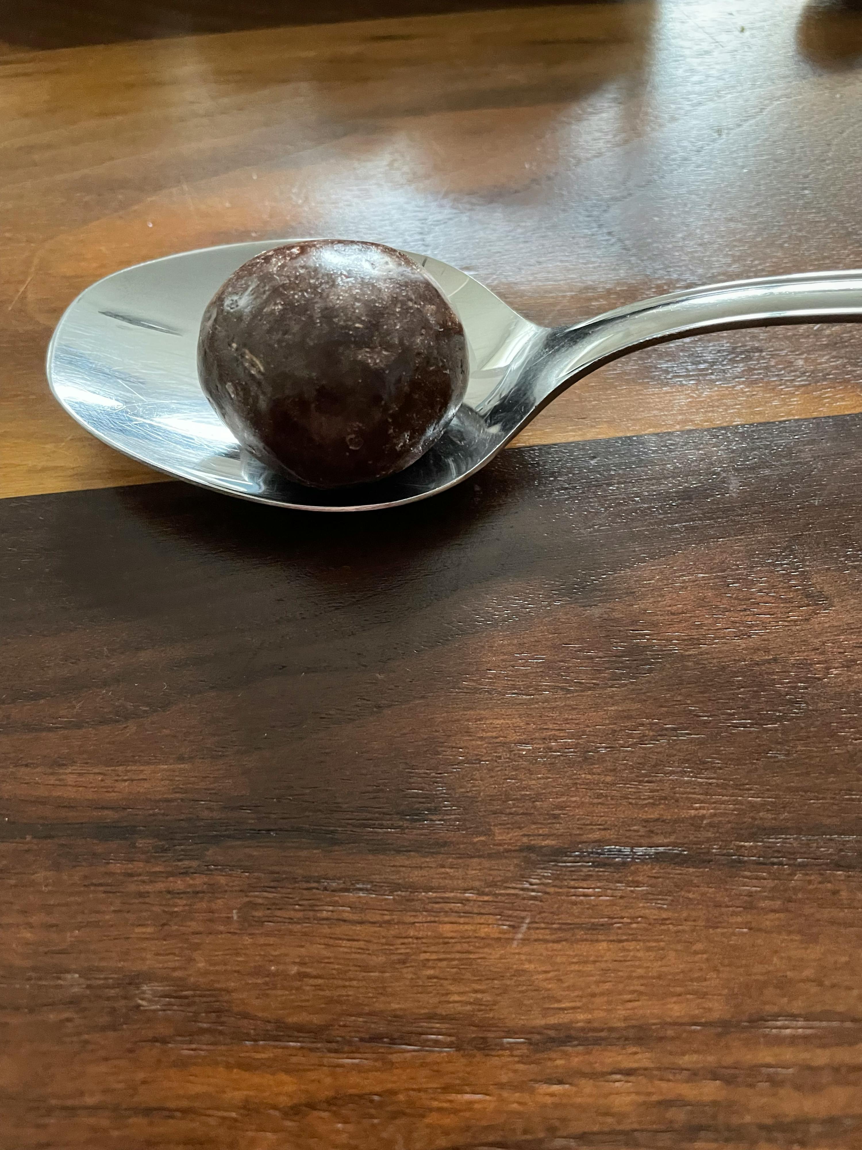 eine Schokoladenkugel liegt auf einem Löffel auf einem Holztisch