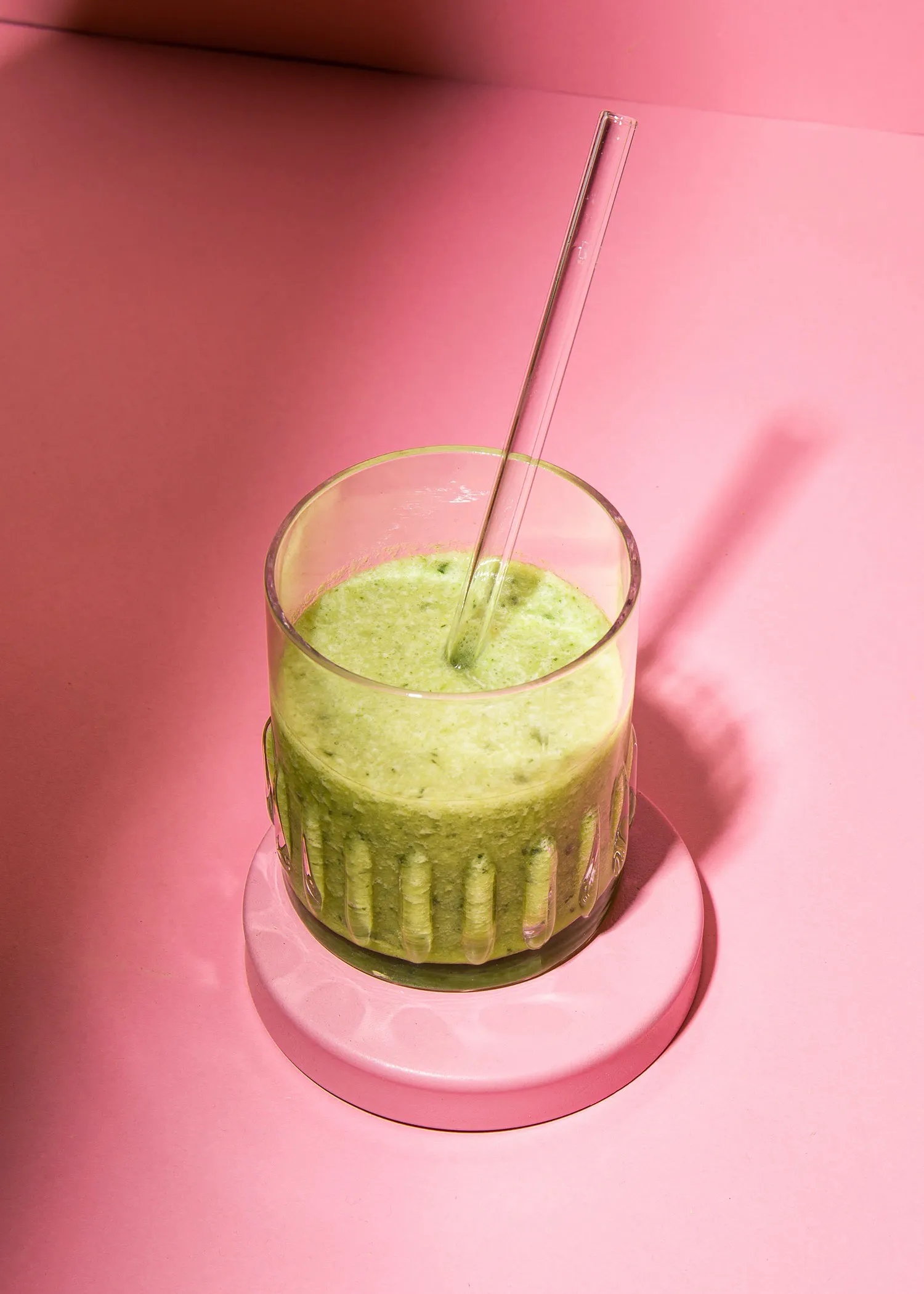 un verre de smoothie vert avec une paille sur une table rose