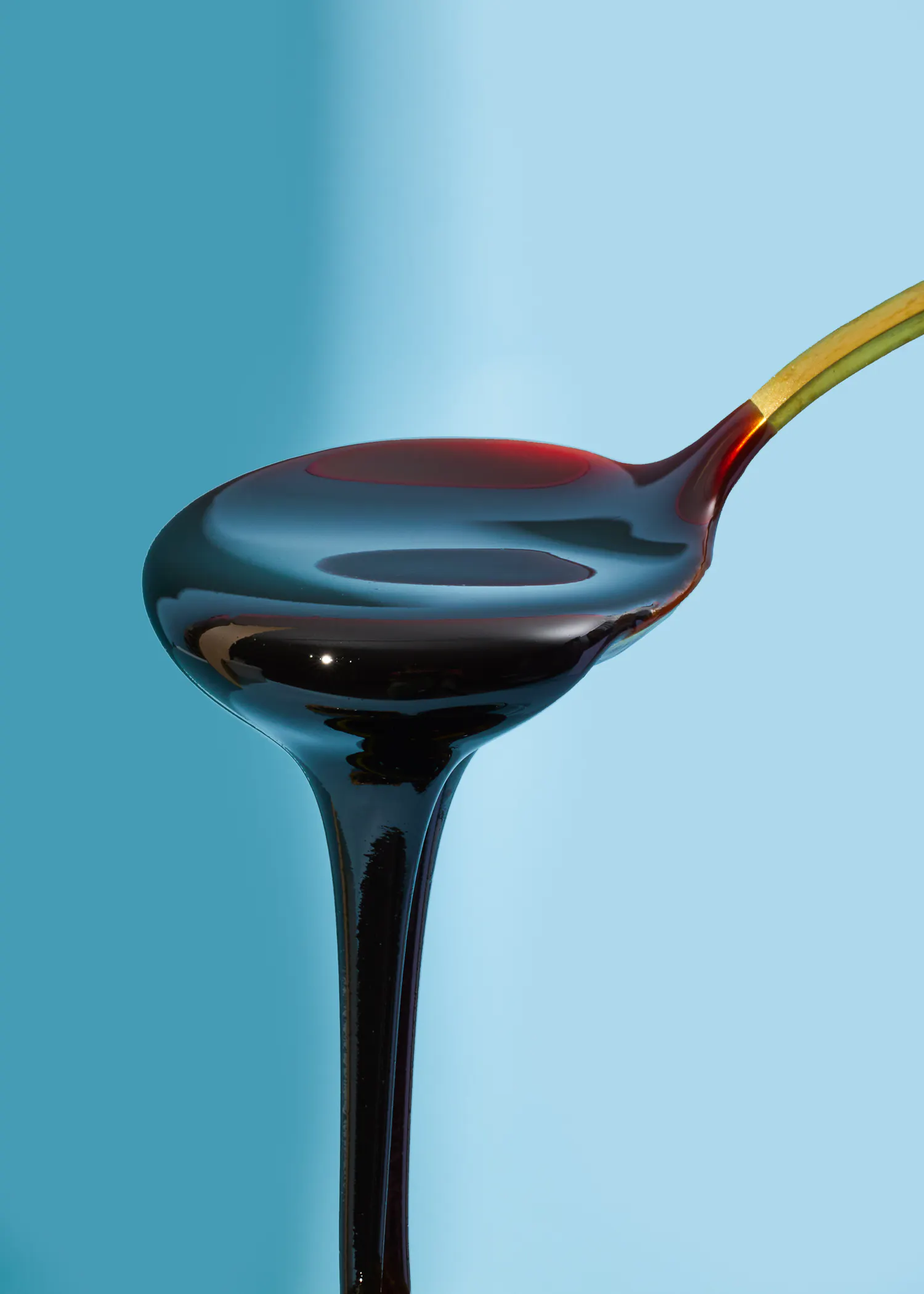a spoon with syrup pouring out of it against a blue background