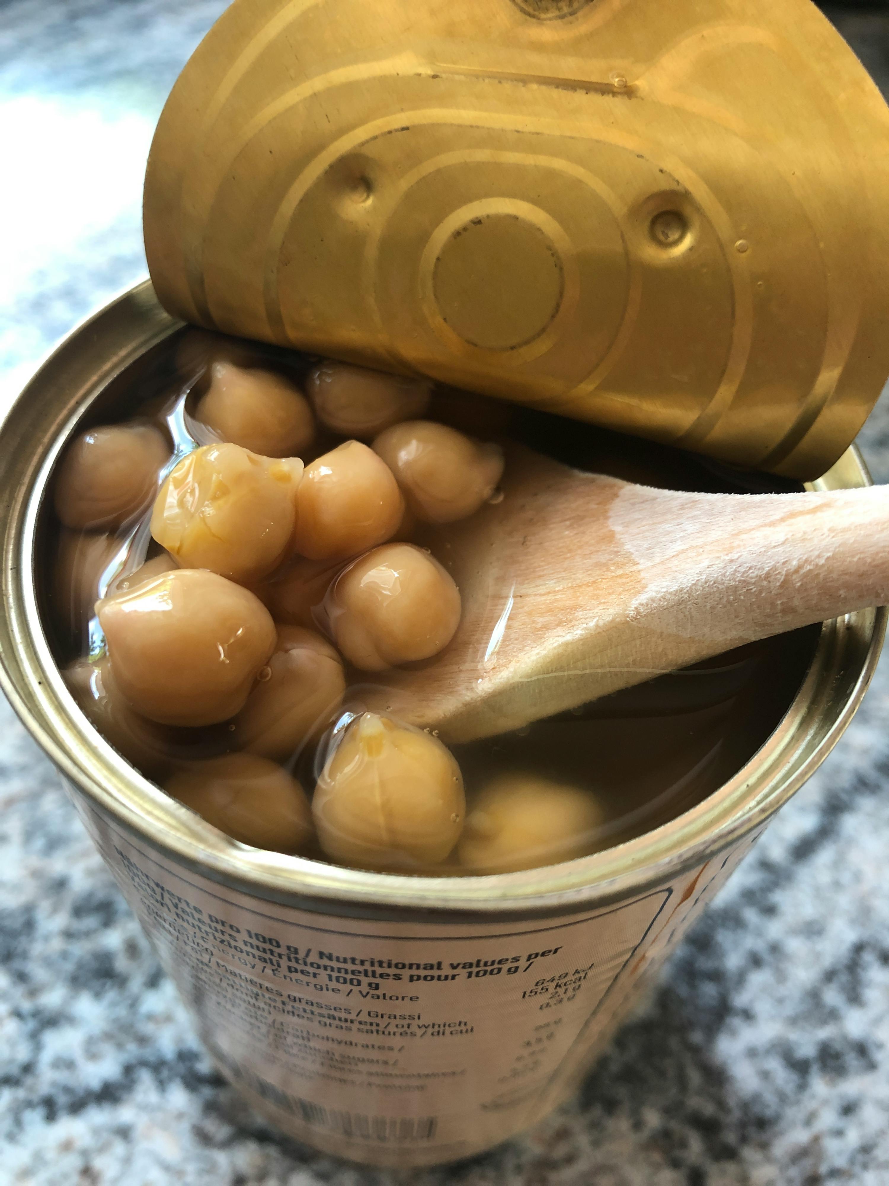 a can of chickpeas with the lid open and a wooden spoon in it