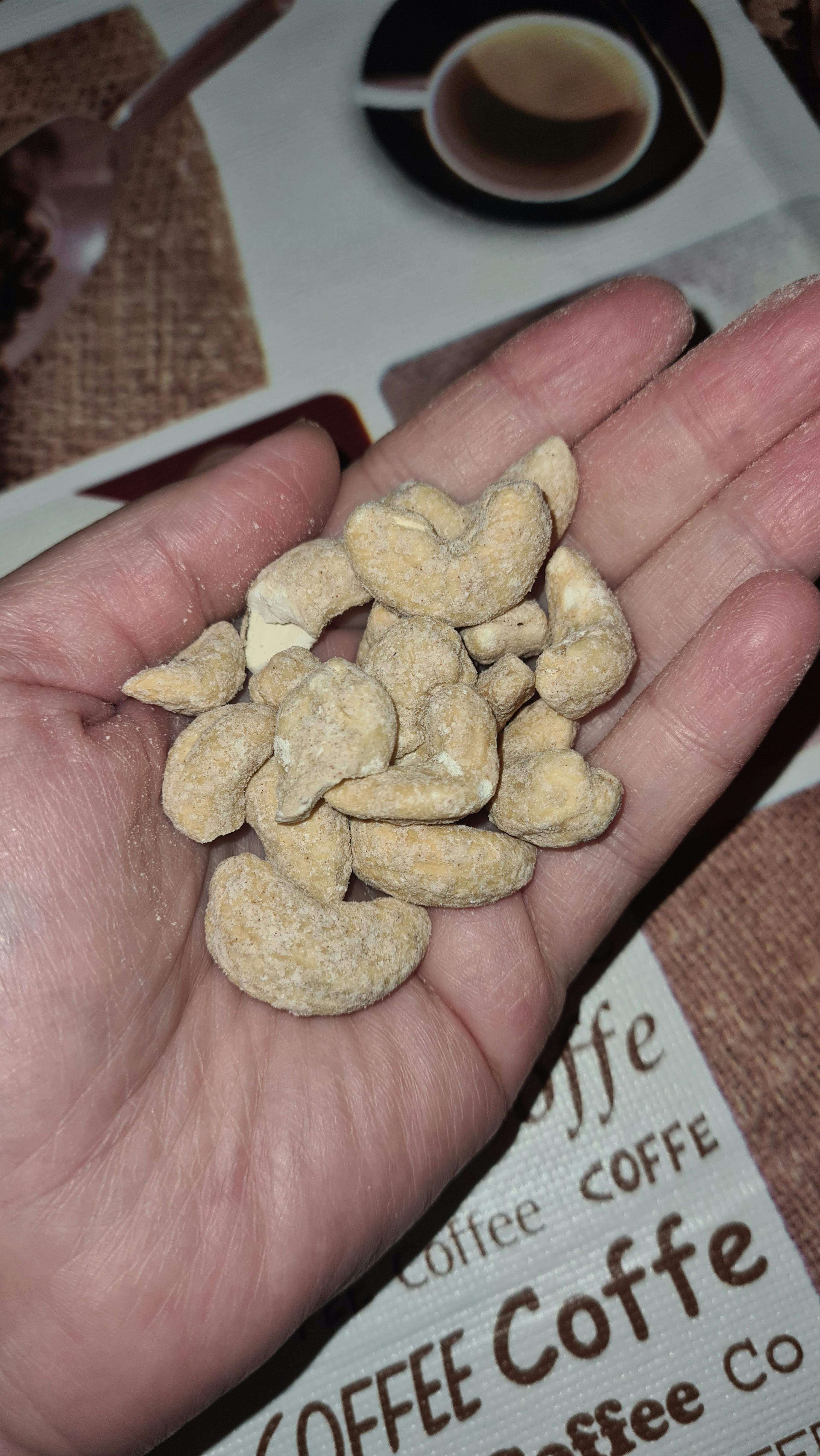 a hand holding a pile of cashews in front of a coffee table cloth