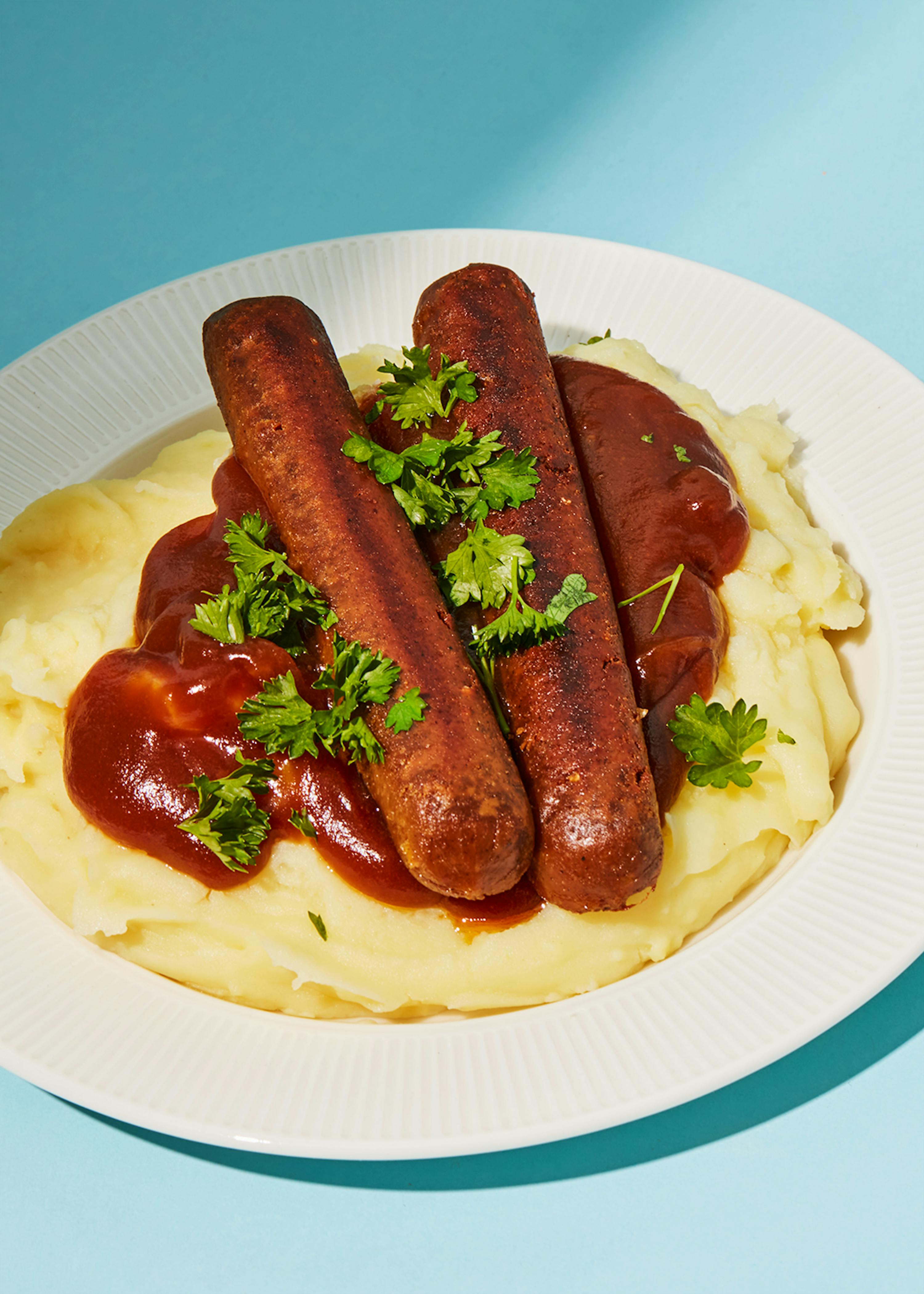 ein weißer Teller mit Kartoffelpüree und Würsten mit Soße