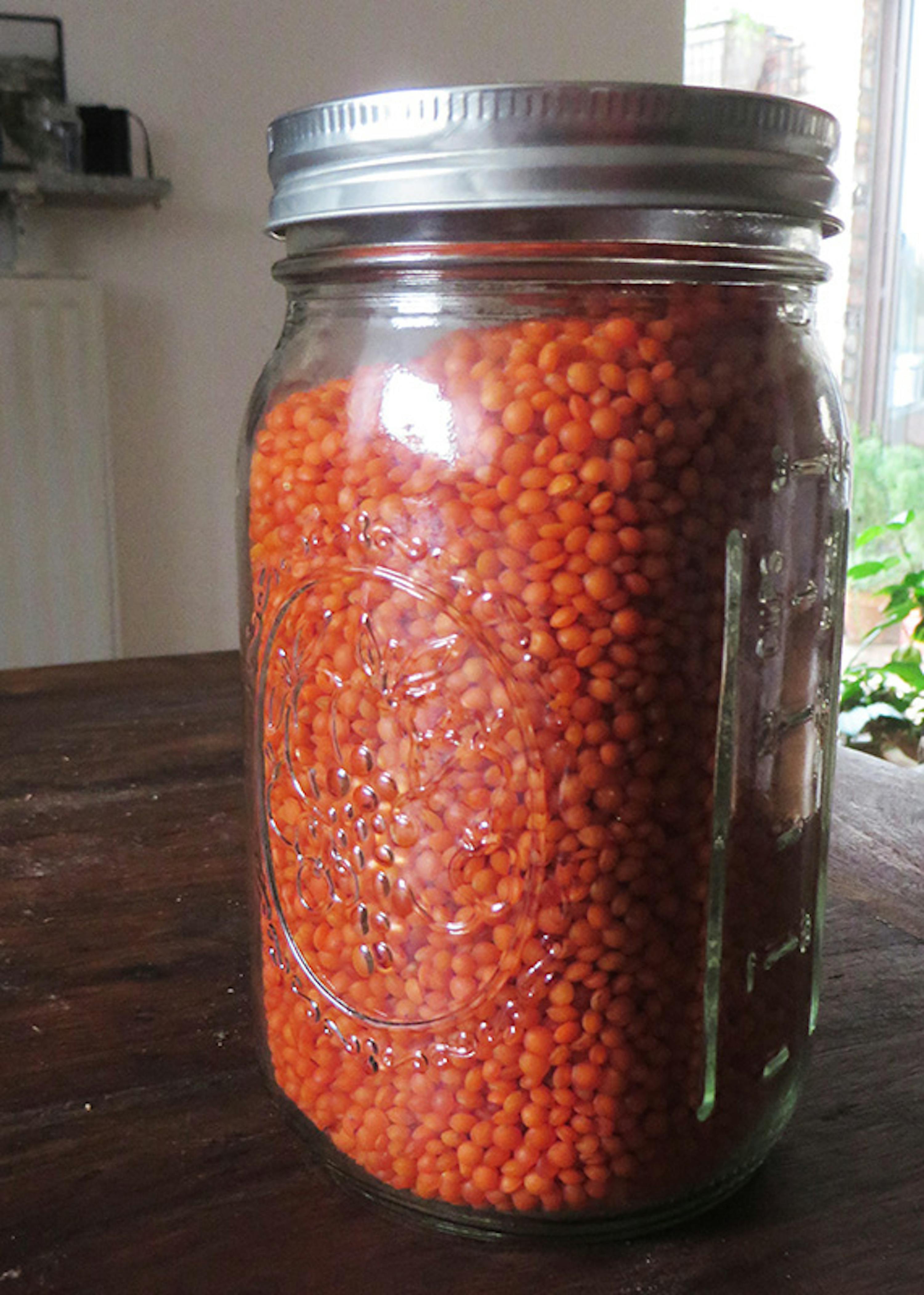 un bocal en verre rempli de lentilles rouges sur une table