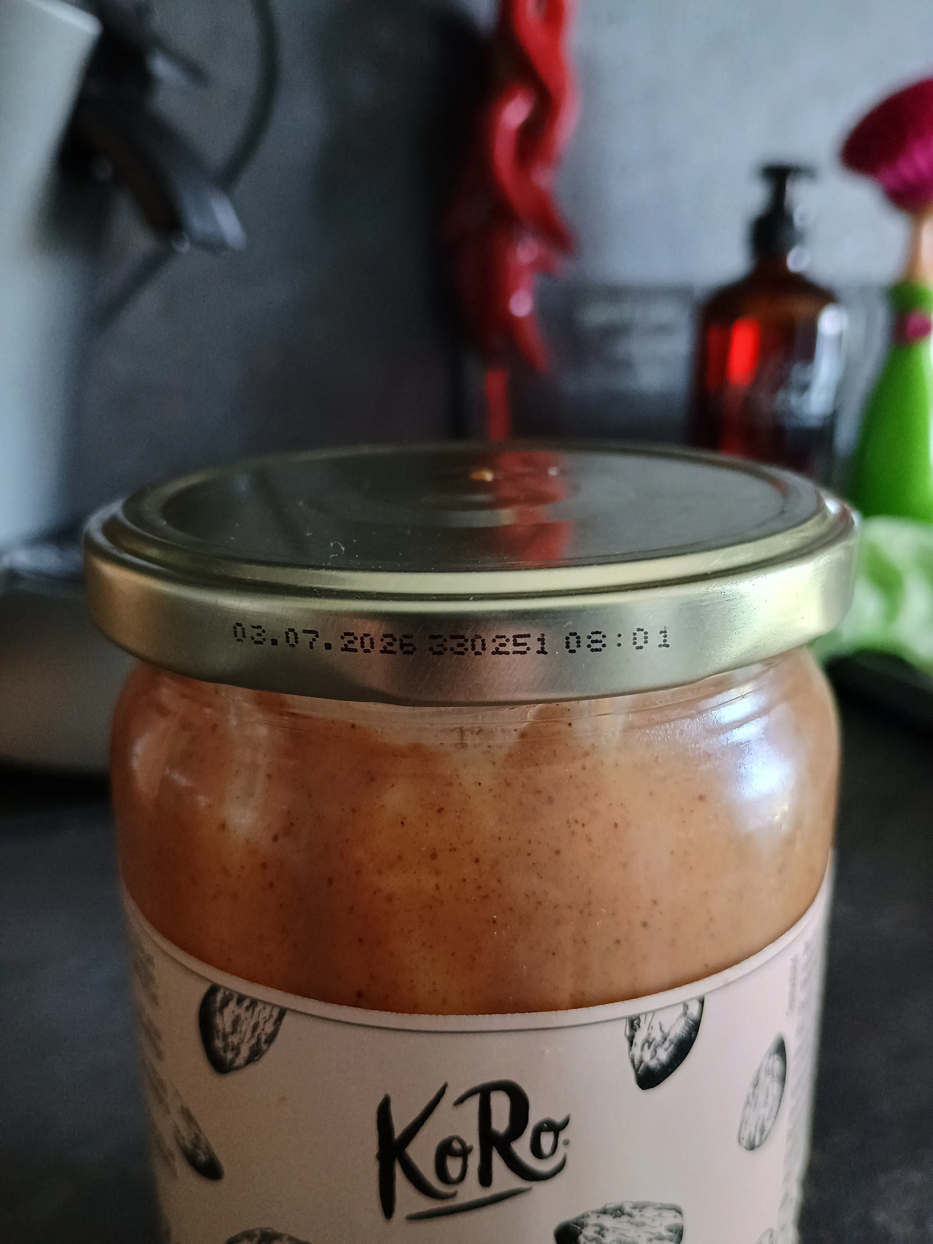 ein liegendes glas nussbutter der marke koro mit goldenem deckel, auf dem das haltbarkeitsdatum 03.07.2026 aufgedruckt ist.
