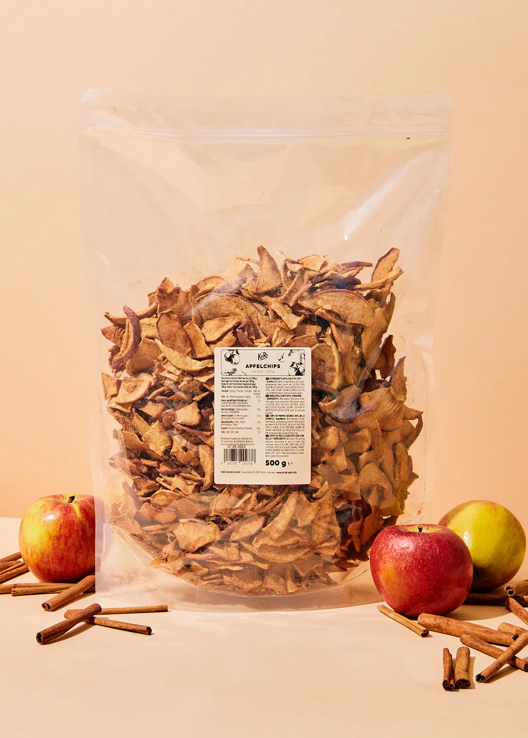 a bag of dried apple slices sits on a table next to apples and cinnamon sticks