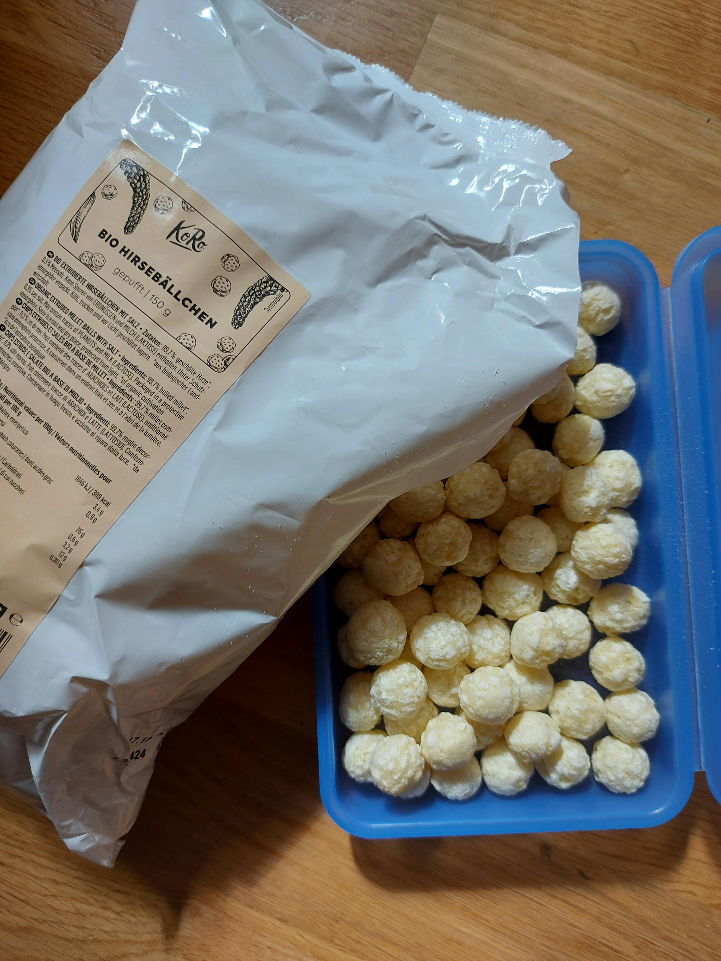 eine Tüte bio-Hirseballen liegt neben einem blauen Plastikbehälter