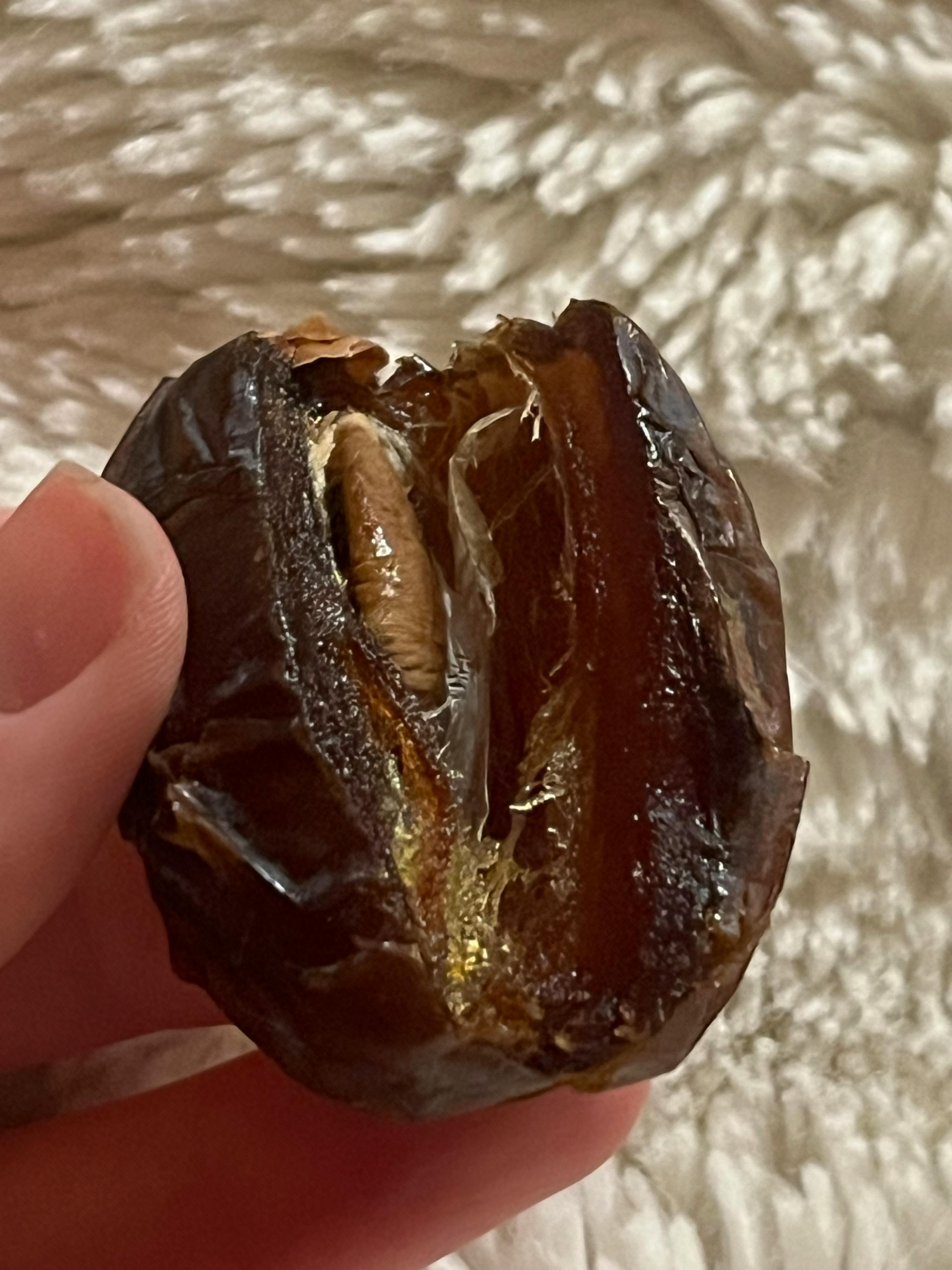 eine aufgeschnittene dattel, die von fingern gehalten wird und ihren kern und das klebrige fruchtfleisch zeigt.