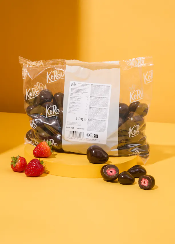 un sac de fraises enrobées de chocolat est assis sur une table jaune