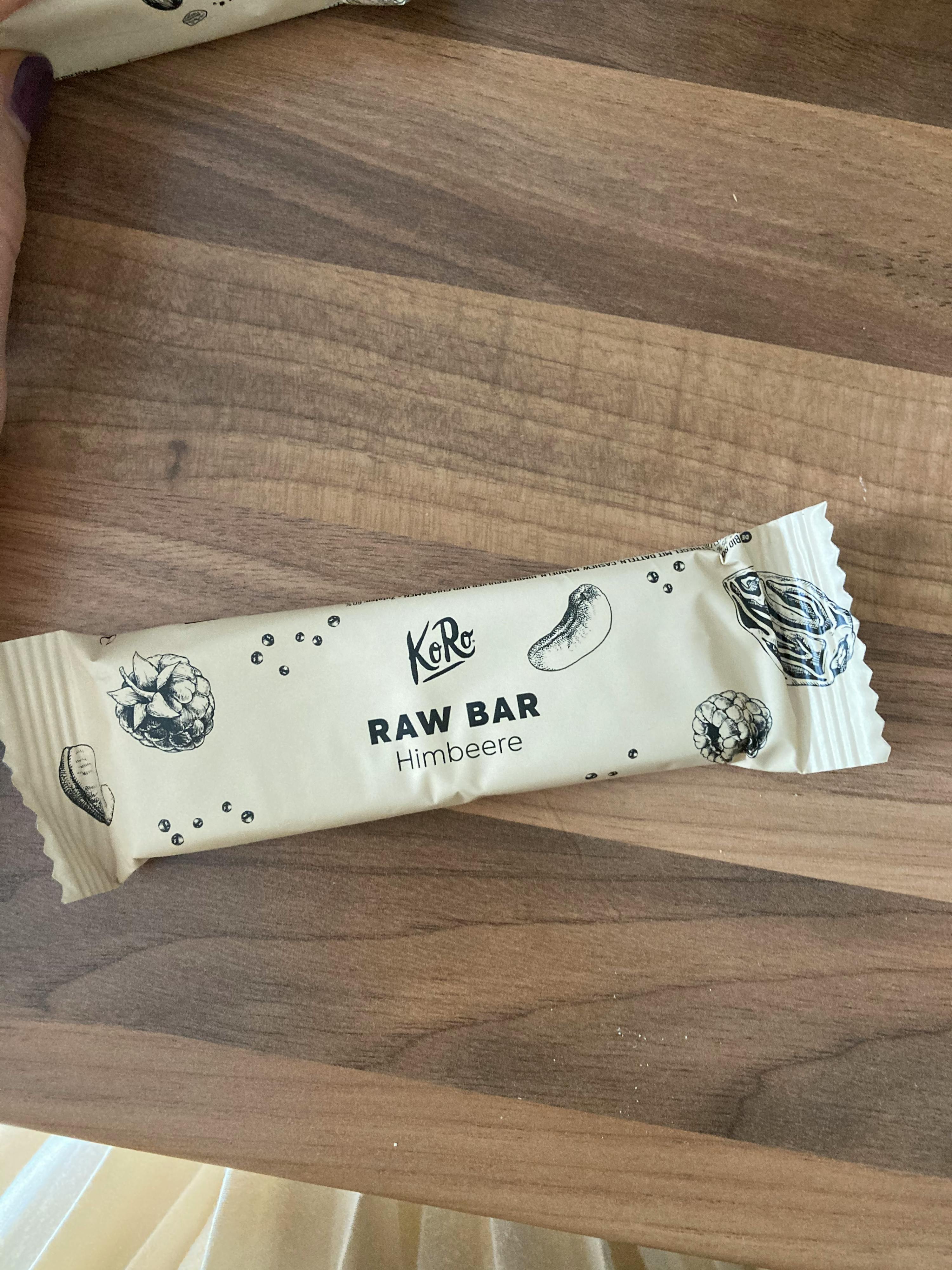 una persona tiene in mano una barretta raw bar di lamponi su un tavolo di legno