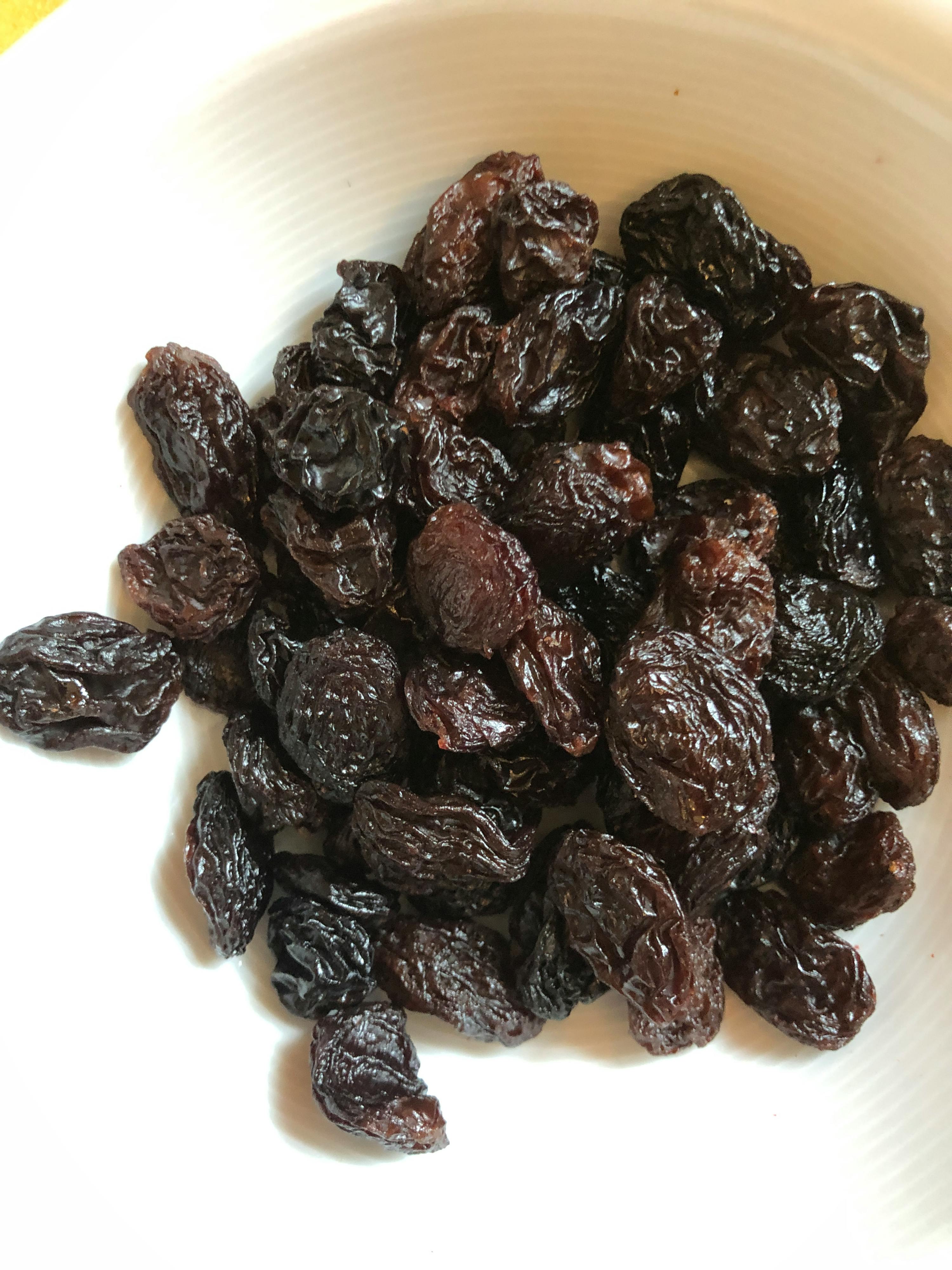 ein weißer Teller mit schwarzen Rosinen auf einem Tisch