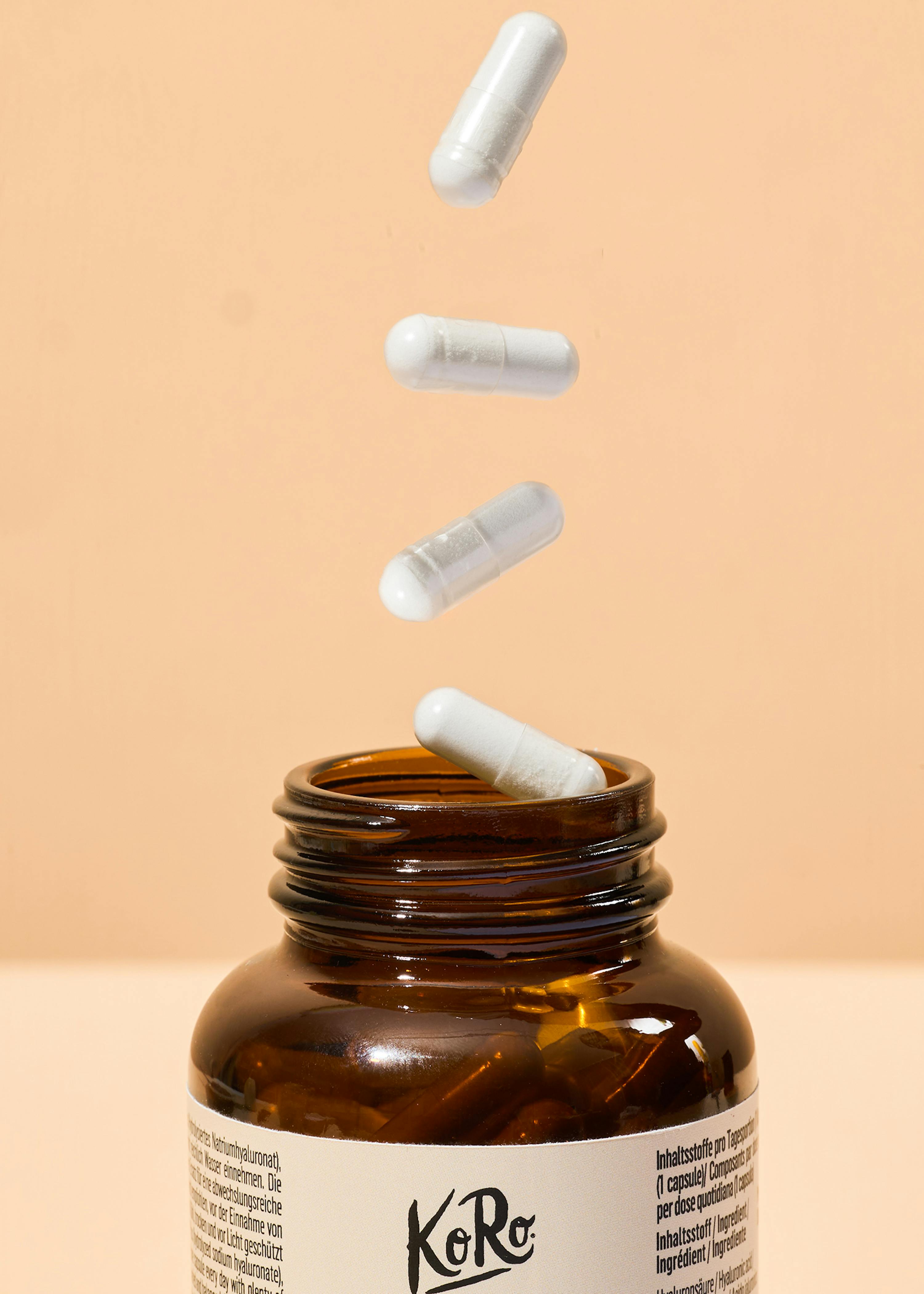 white capsules falling out of a bottle of koro