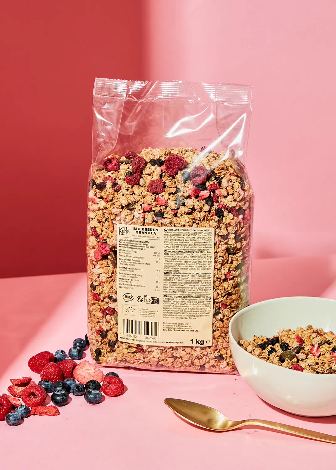 un sac de granola avec des baies et une cuillère à côté d' un bol de granola
