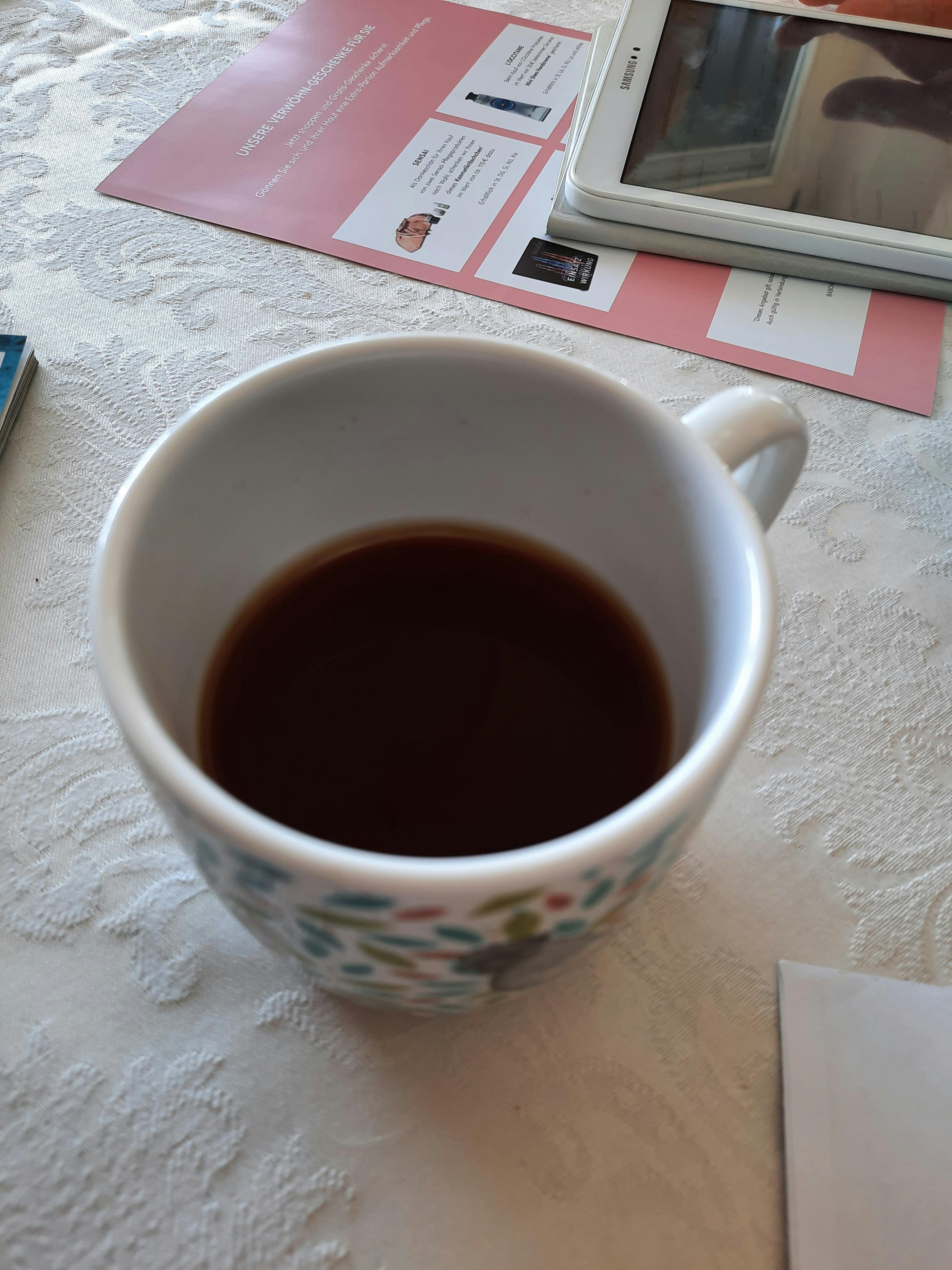 una tazza di caffè seduta su un tavolo accanto a un samsung