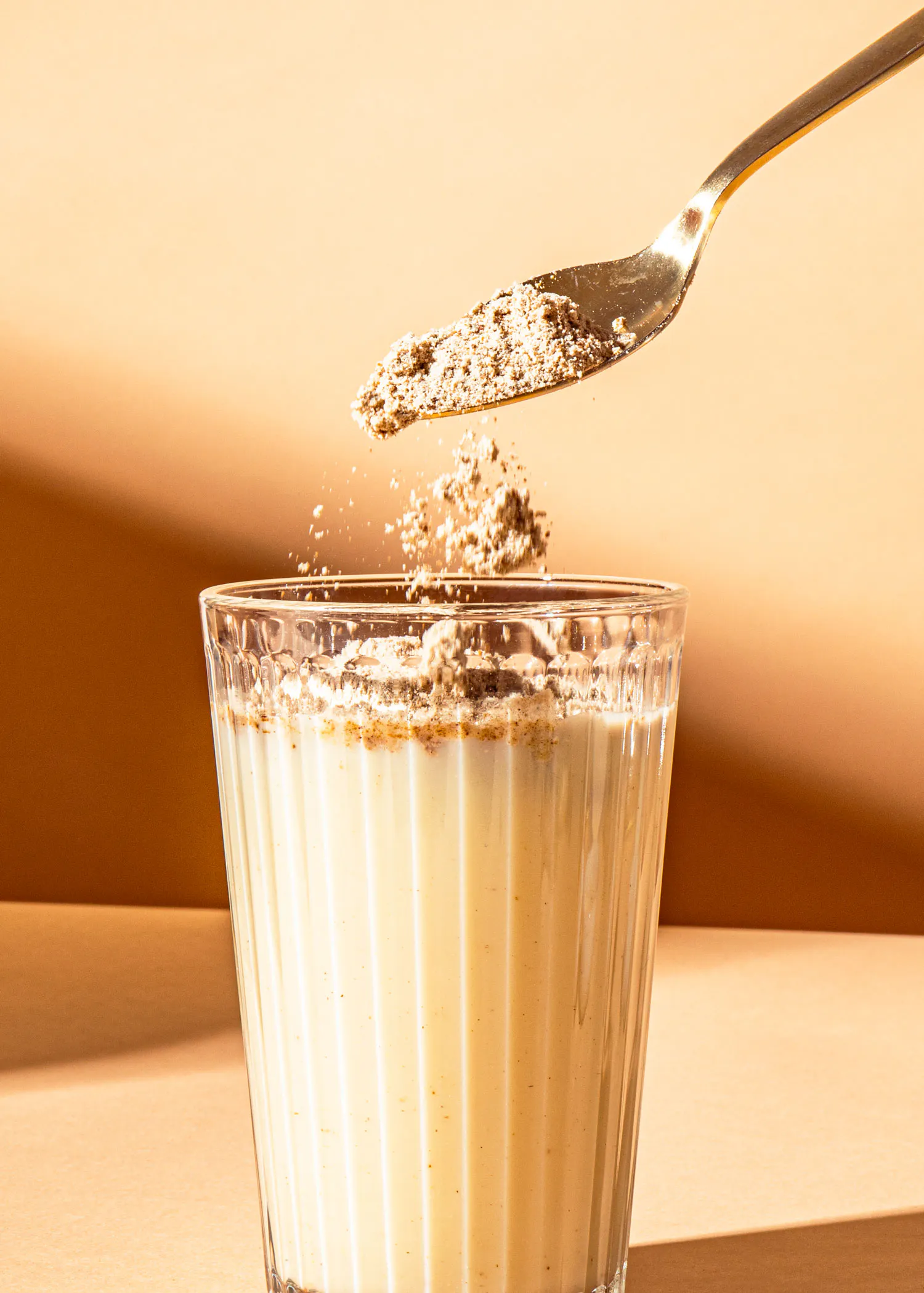 une cuillère verse du poudre dans un verre de boisson
