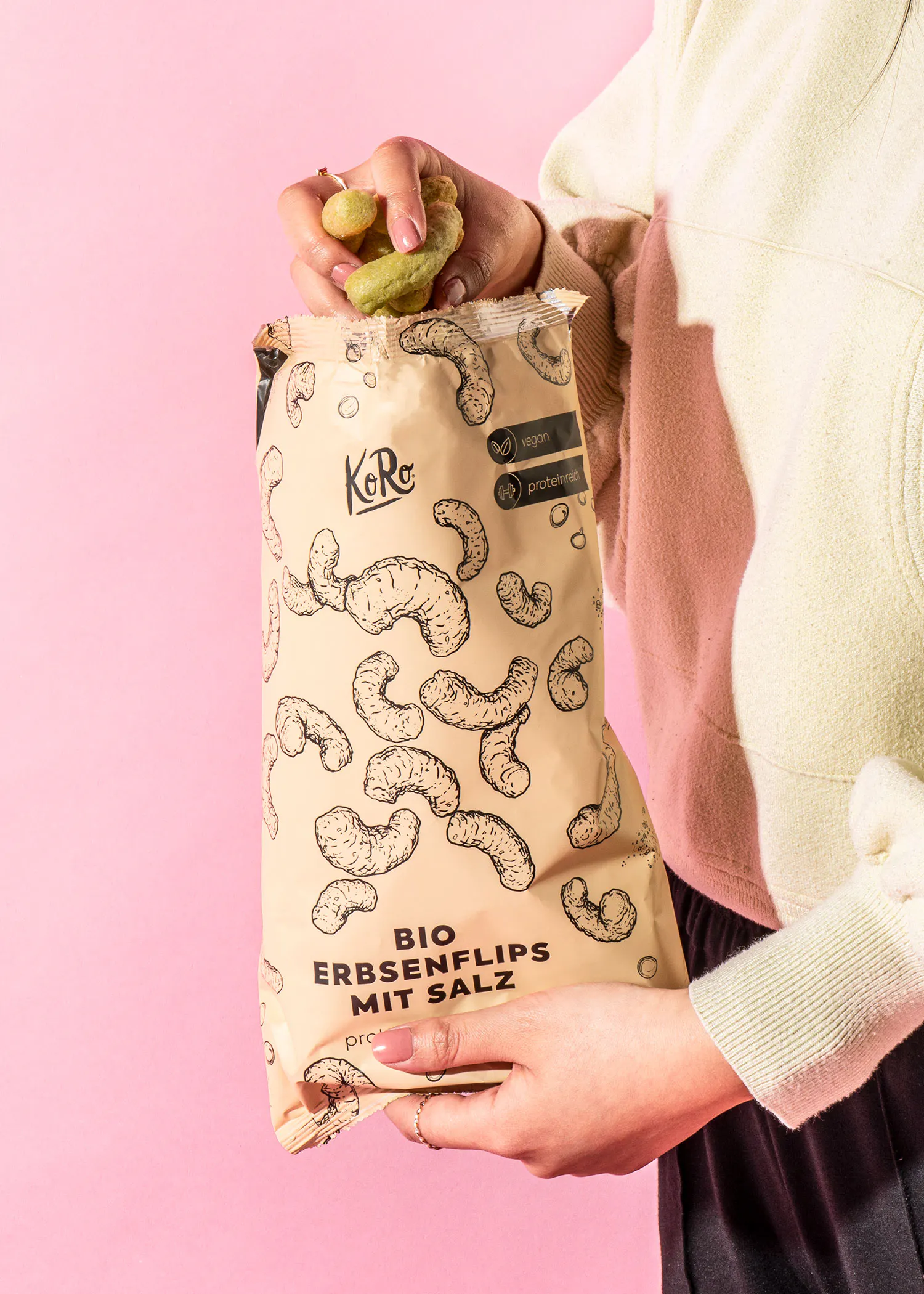 eine frau hält einen beutel bio erbsenflips mit salz in der hand