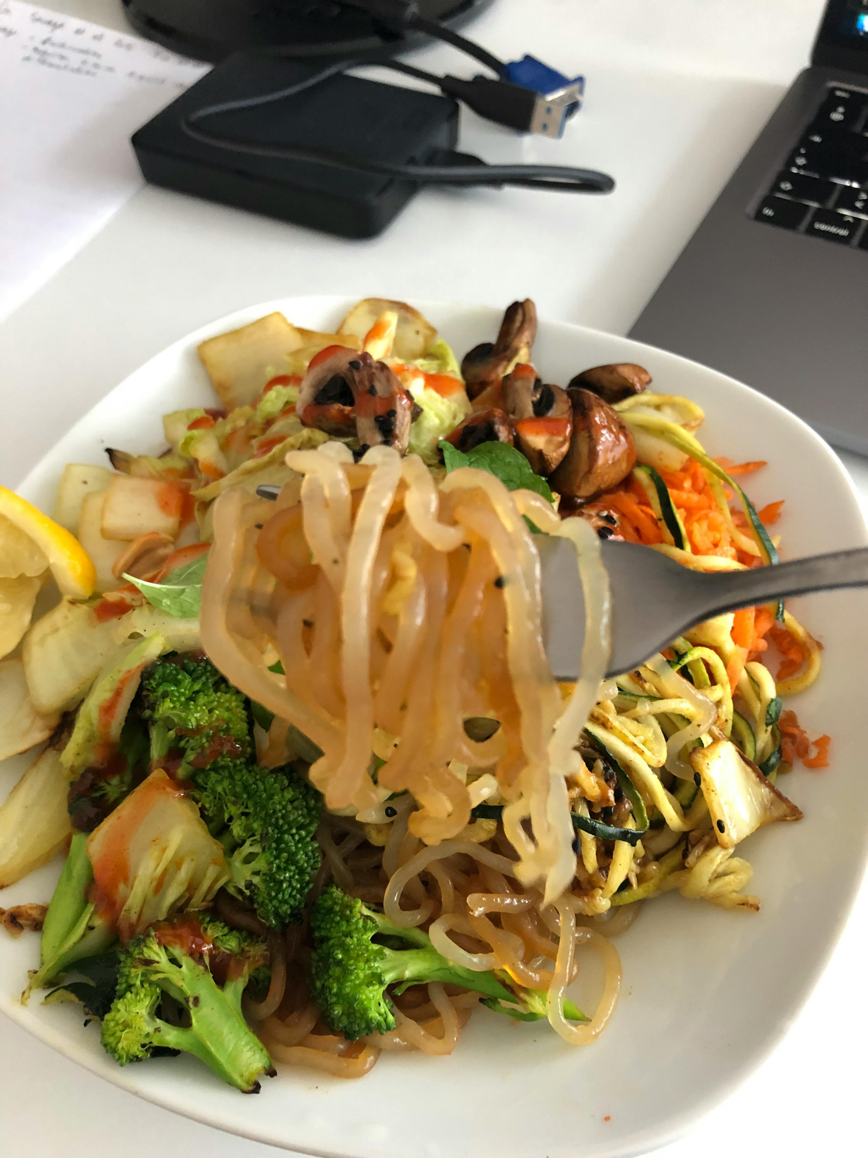 a bowl of noodles and vegetables is being eaten with a fork
