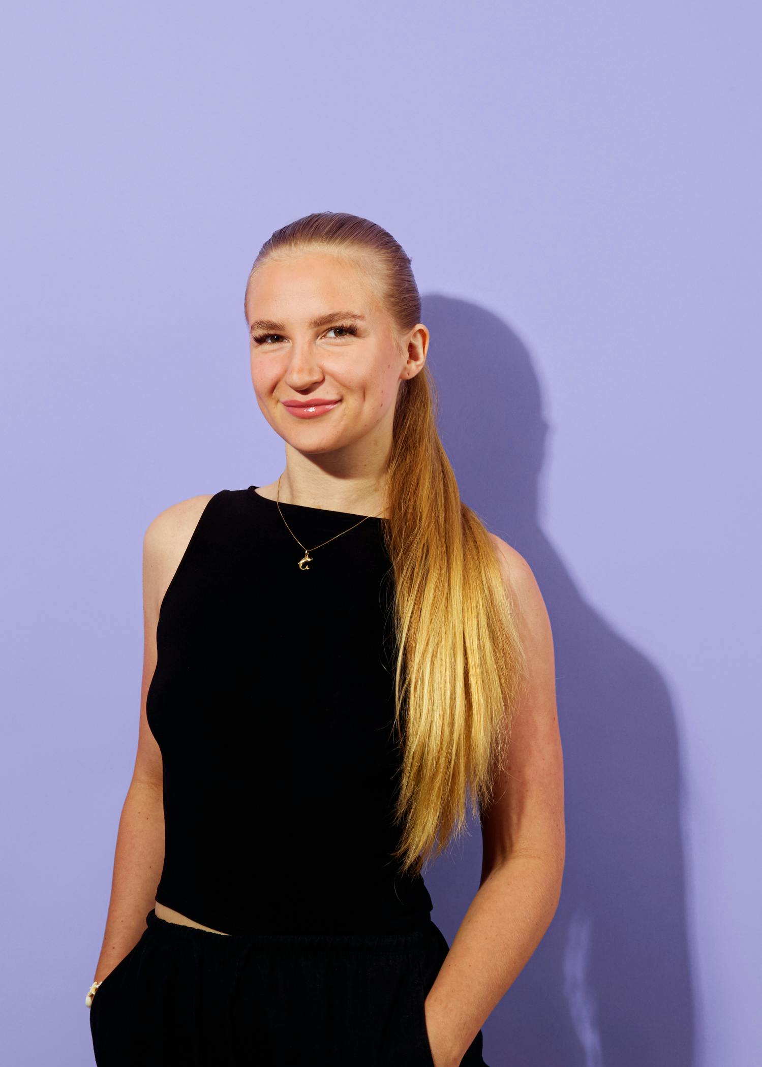 a woman wearing a black top and a gold necklace with the letter g on it