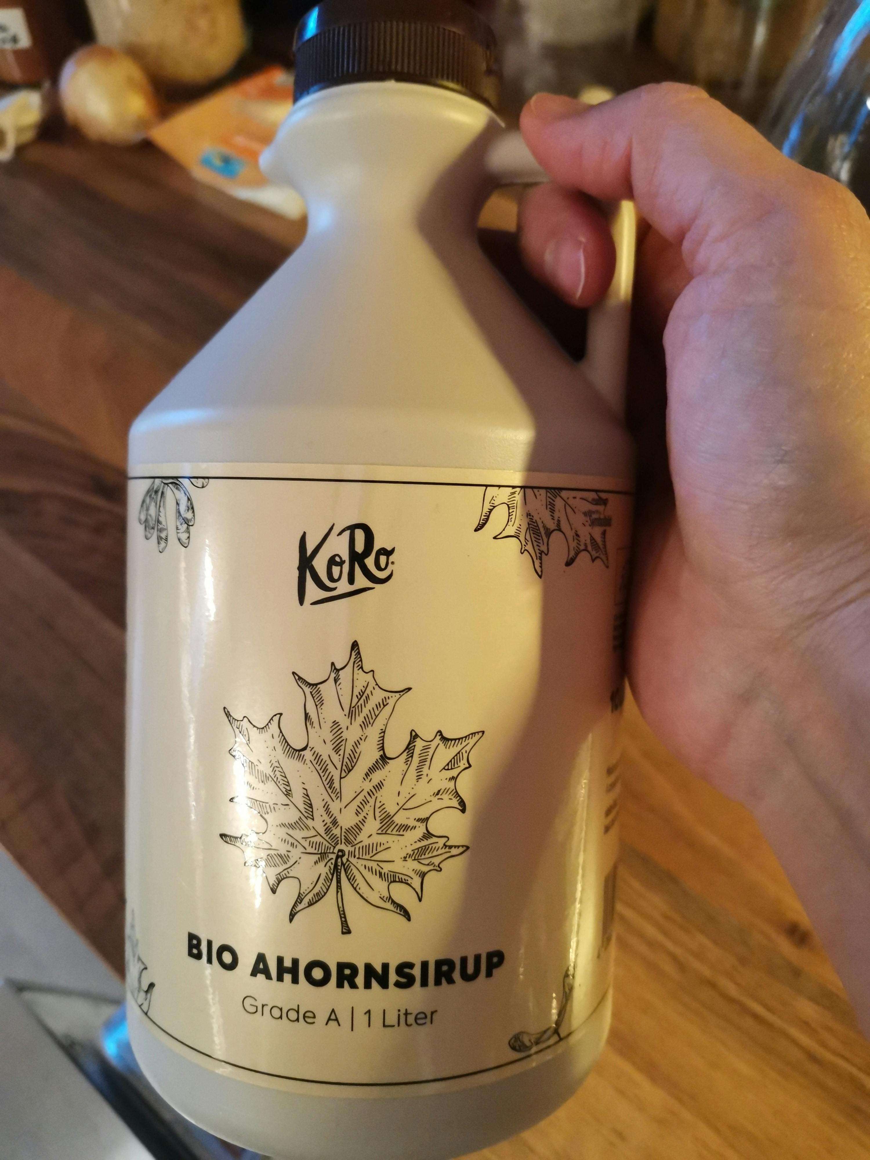 a person is holding a bottle of koro bio ahornsirup