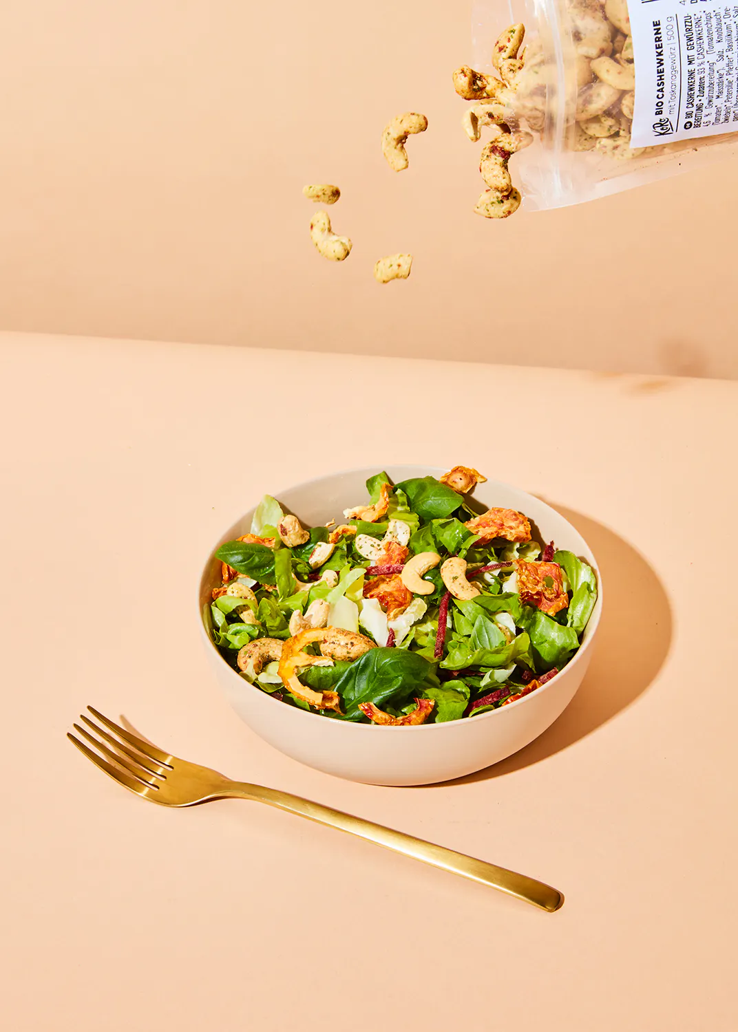 un sac de noix de cajou est versé sur une salade avec une fourchette