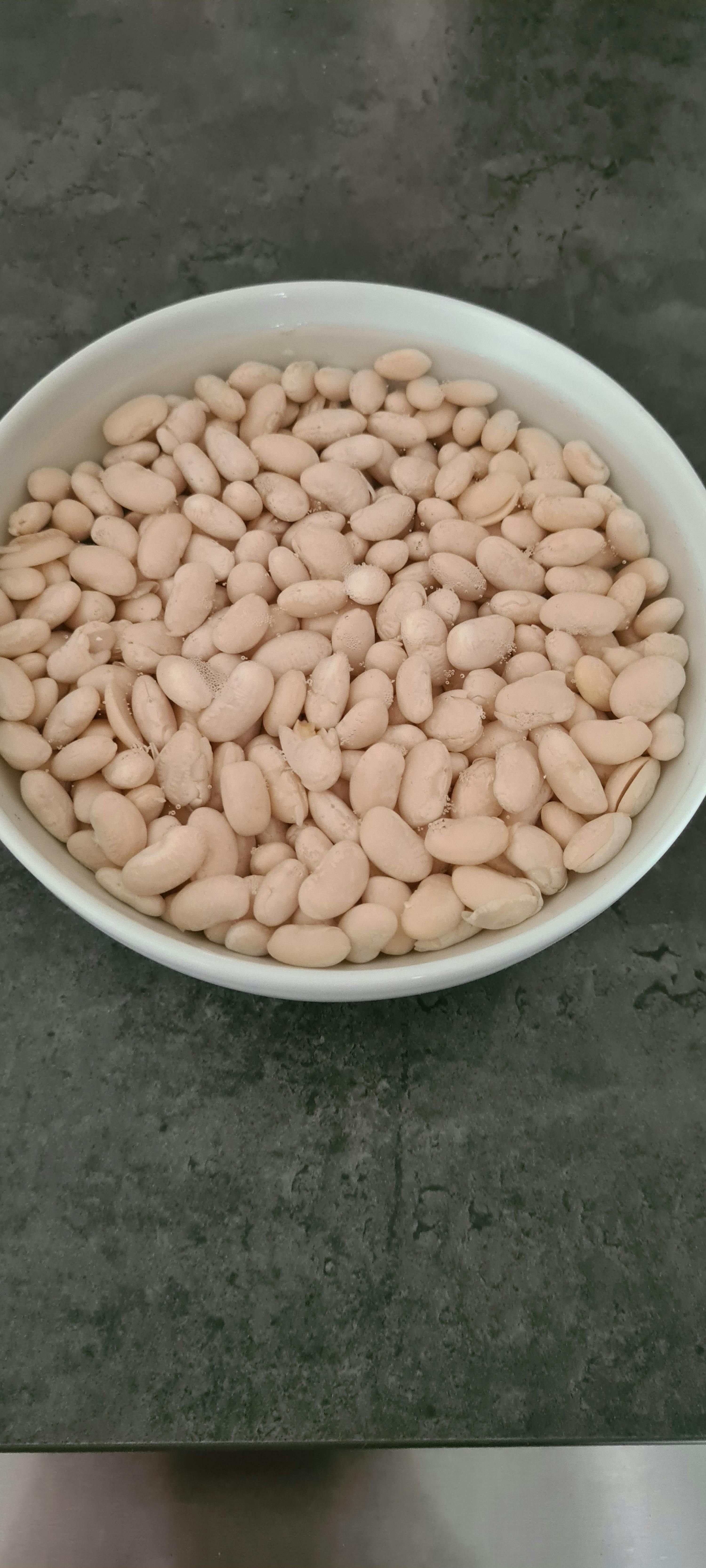 eine weiße Schüssel gefüllt mit weißen Bohnen auf einem Tisch