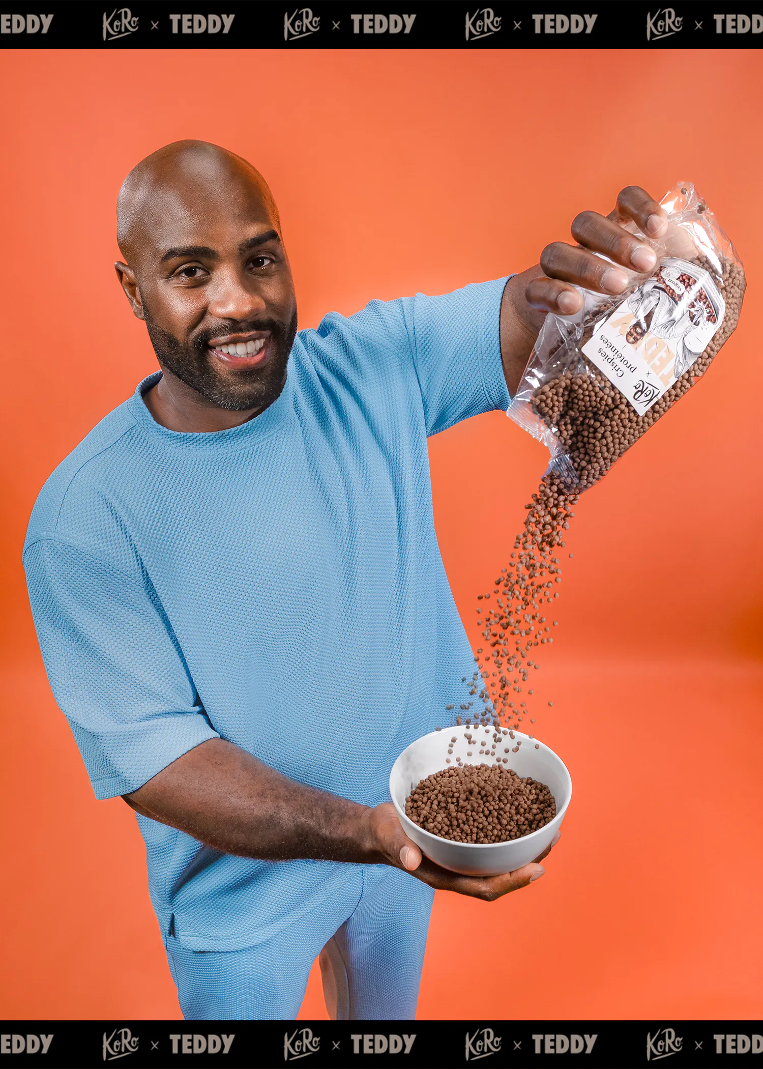 un homme souriant, vêtu de bleu clair, verse des crispies protéinées au chocolat d'un sachet transparent dans un bol blanc sur un fond orange.