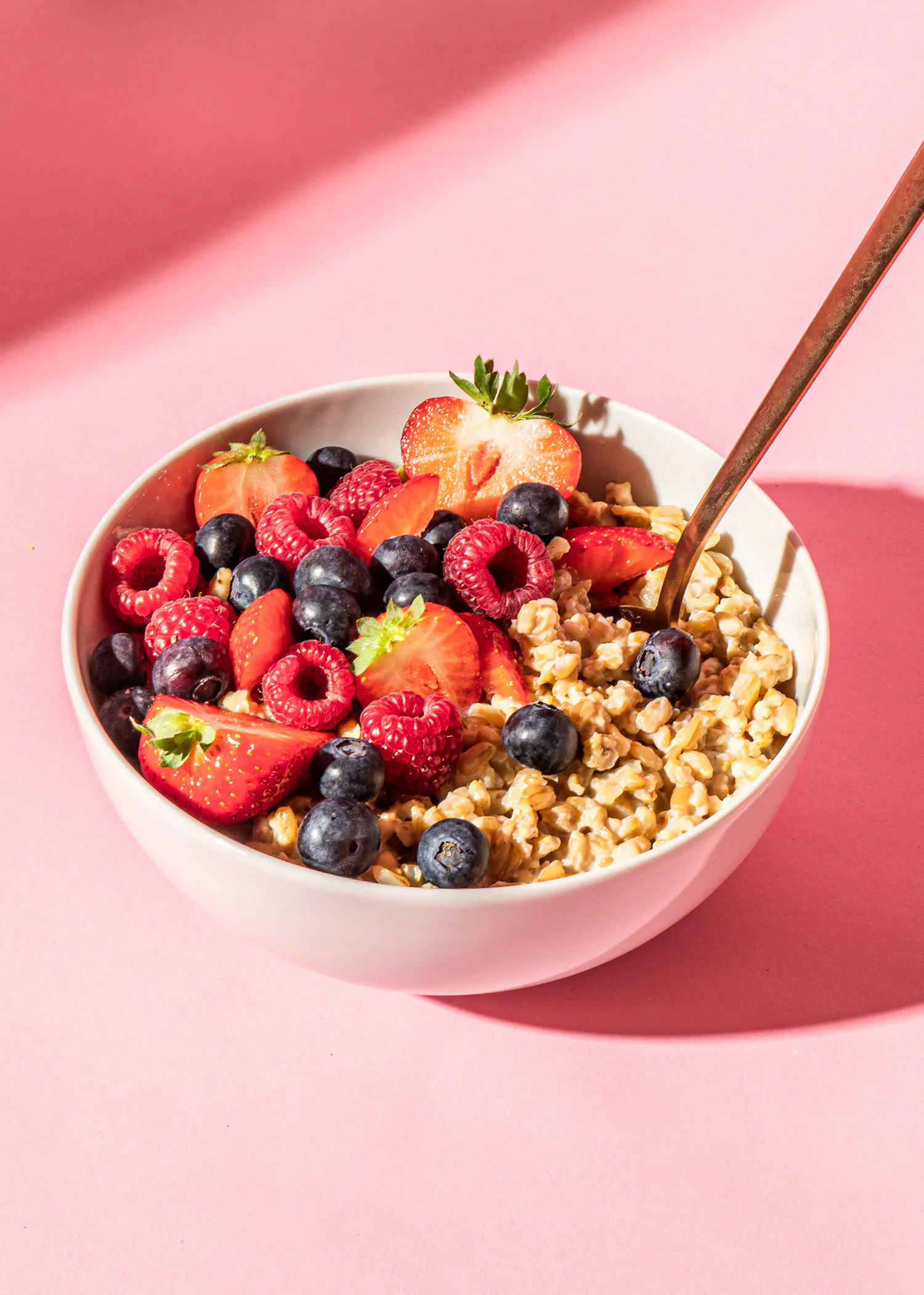 a bowl of oatmeal with blueberries raspberries and strawberries on a pink background