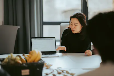 una mujer se sienta en una mesa frente a una computadora portátil con una pantalla que dice general costs & rates