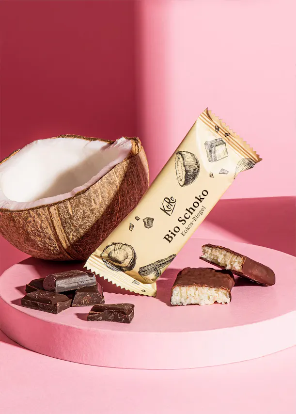 une barre de chocolat bio schoko est posée sur une surface rose à côté d' une noix de coco