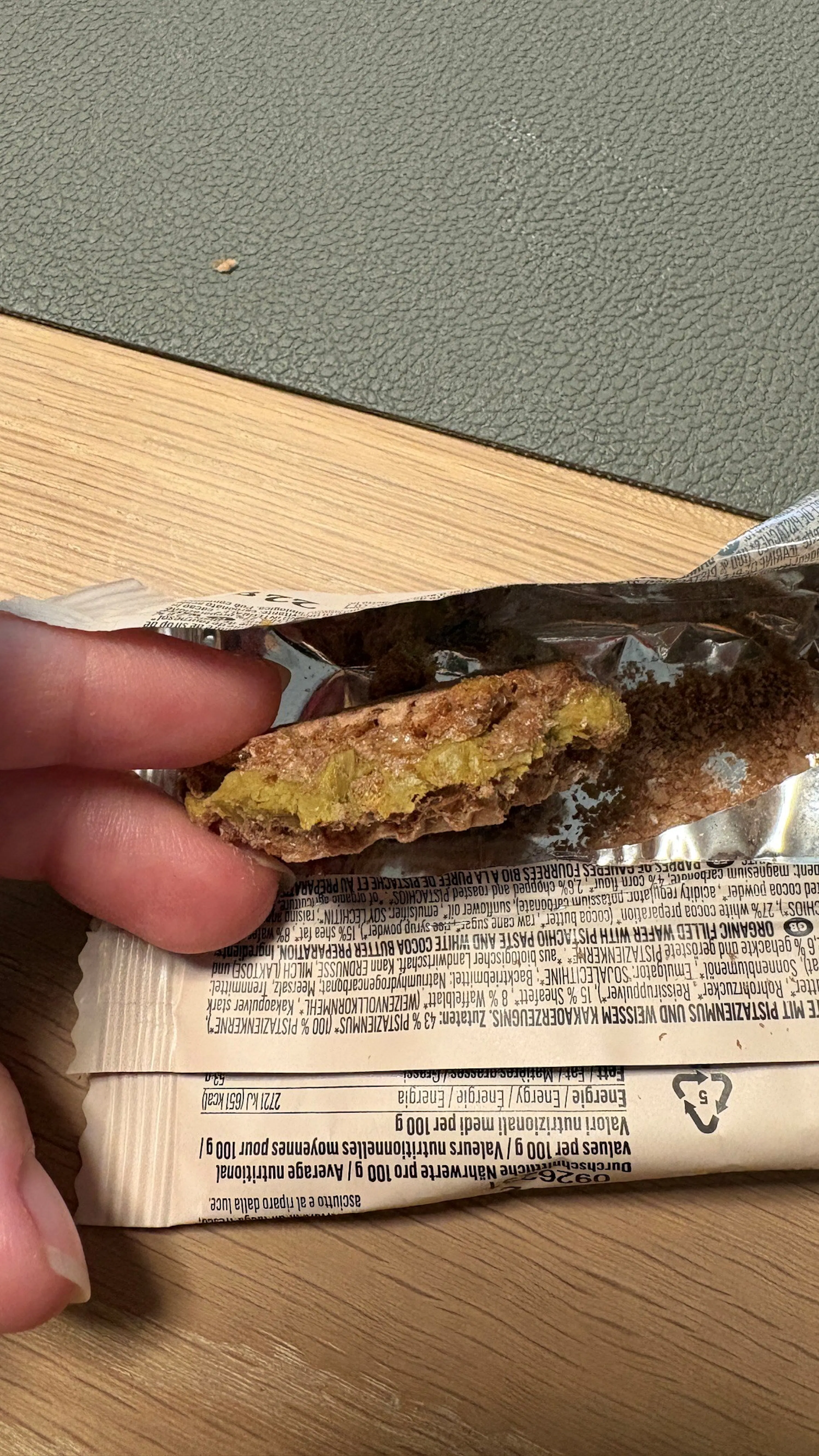 una barretta di cioccolato parzialmente scartata con un ripieno verde di pistacchio visibile.