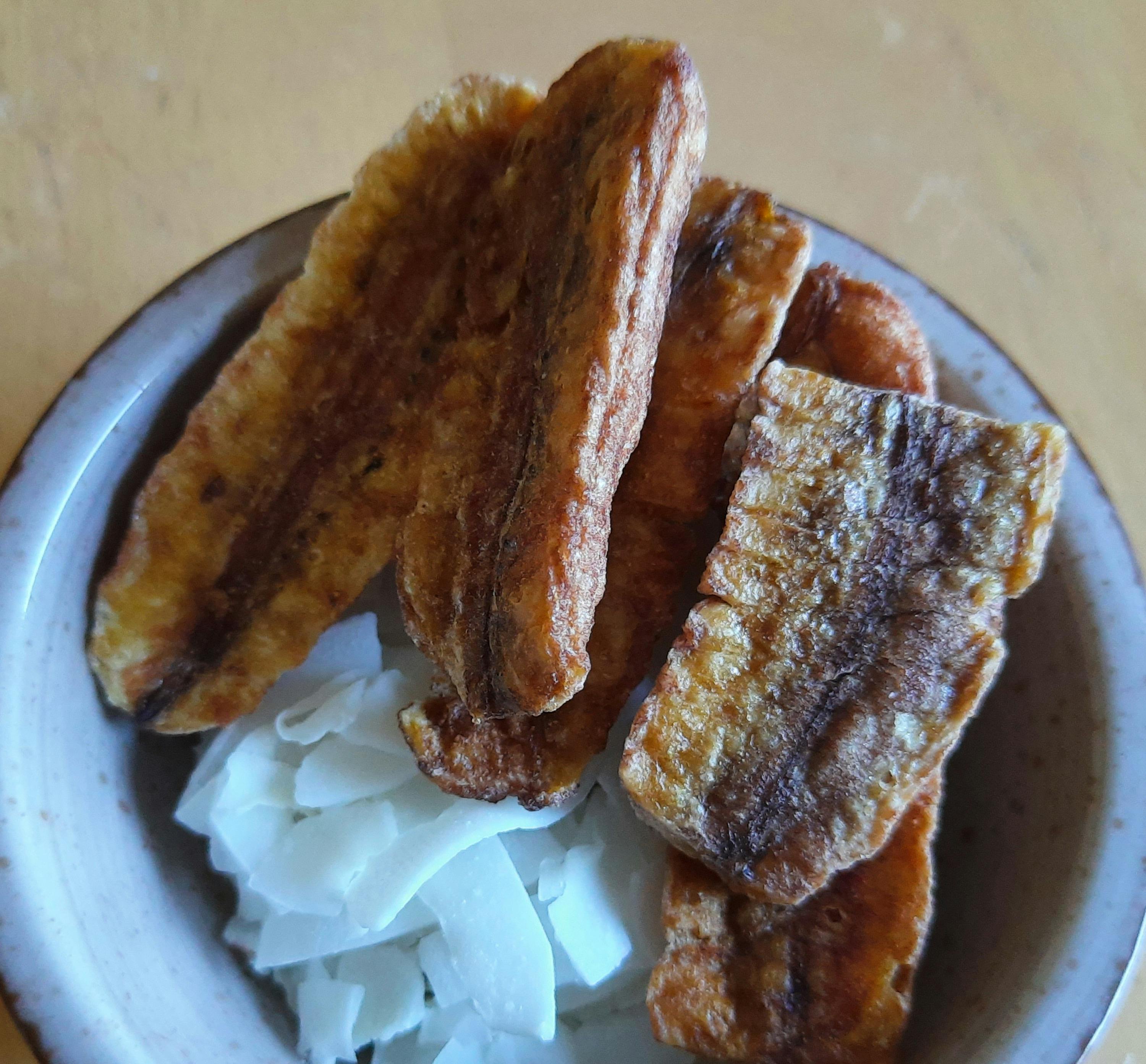 a bowl of fried bananas and coconut chips on a table